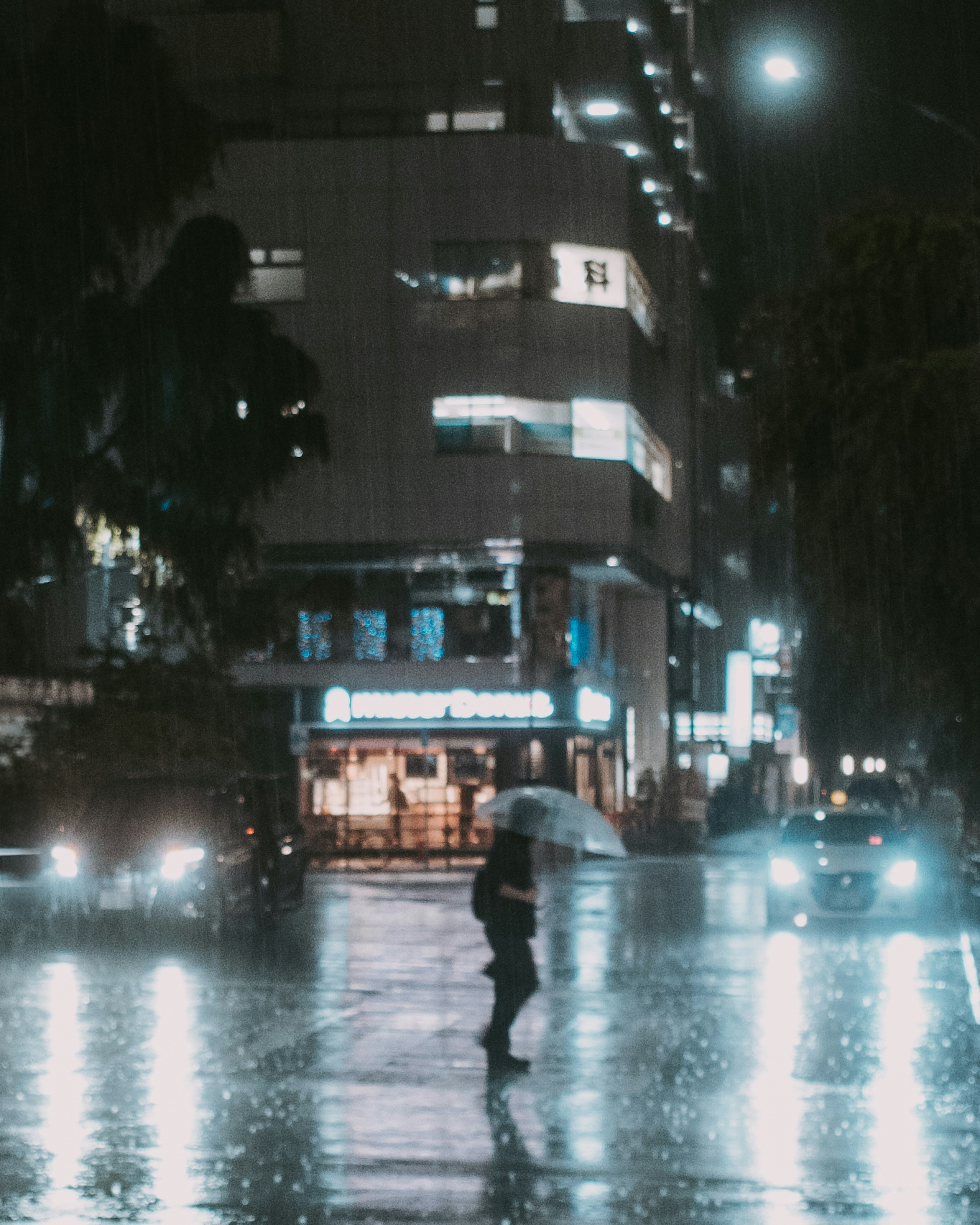 A person walking with an umbrella in the rain with city lights reflecting on the wet pavement