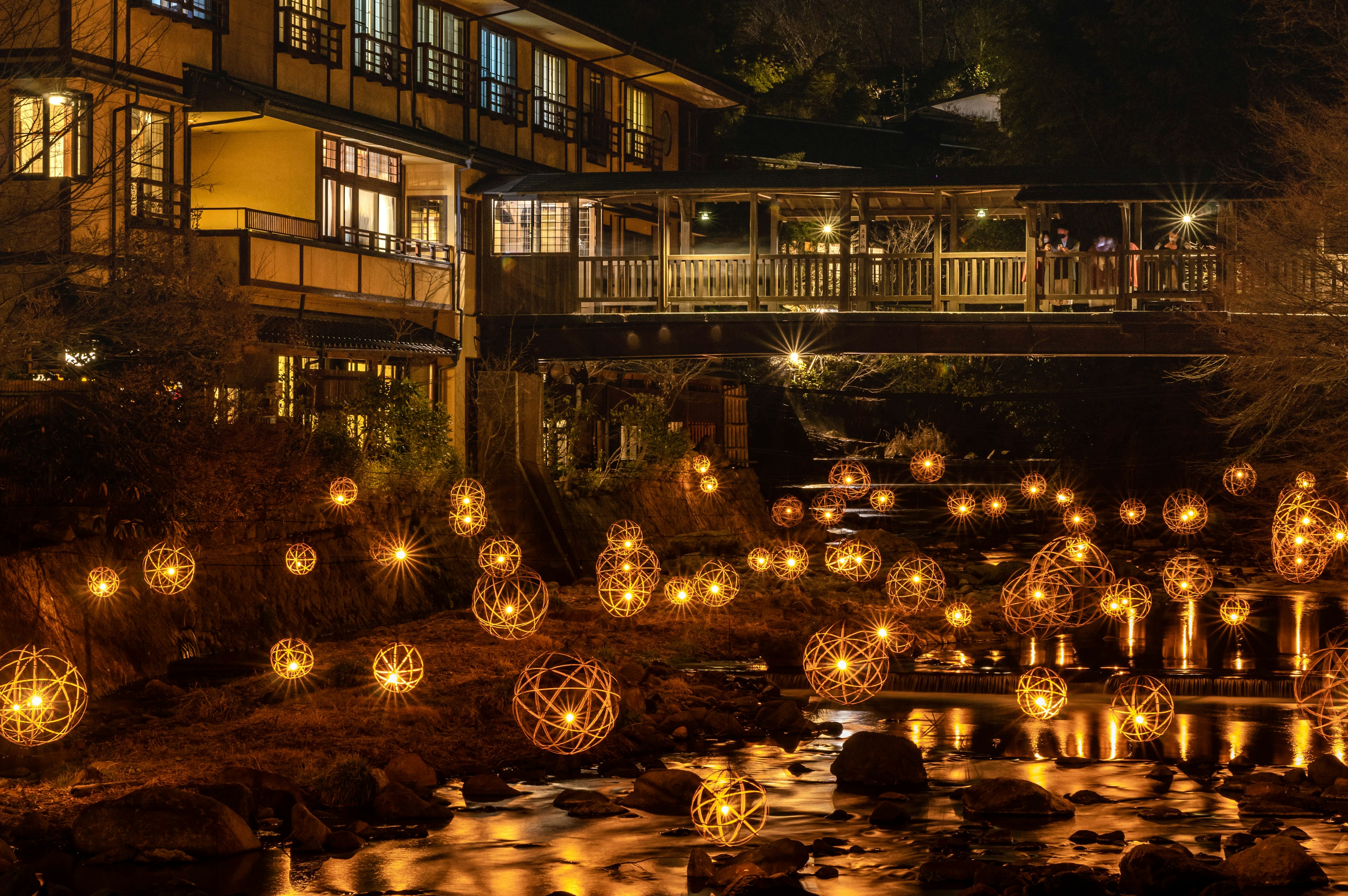 Vista panoramica di lanterne luminose che galleggiano su un fiume con un ponte di notte