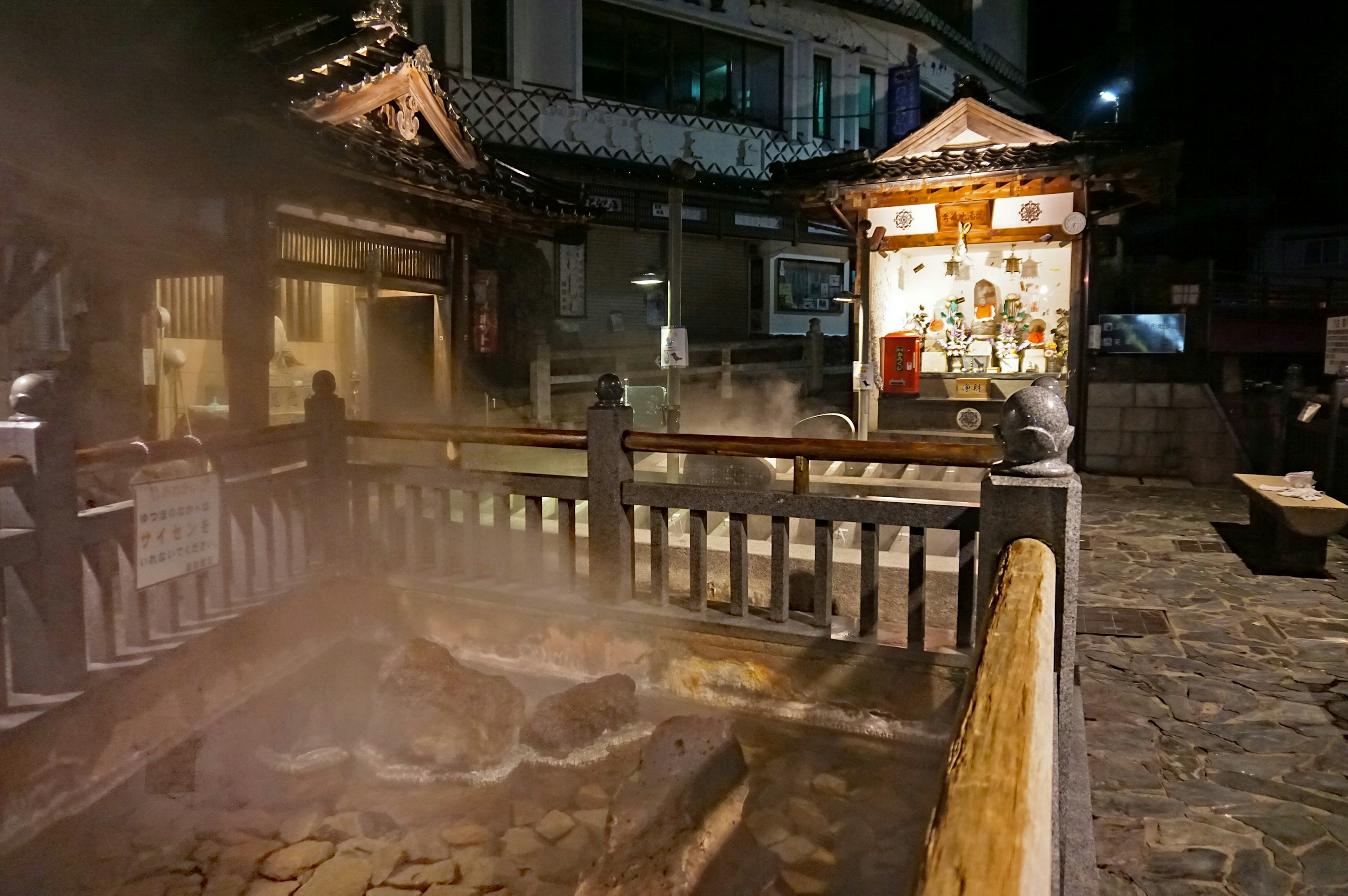 Outdoor hot spring with steam at night surrounded by traditional architecture