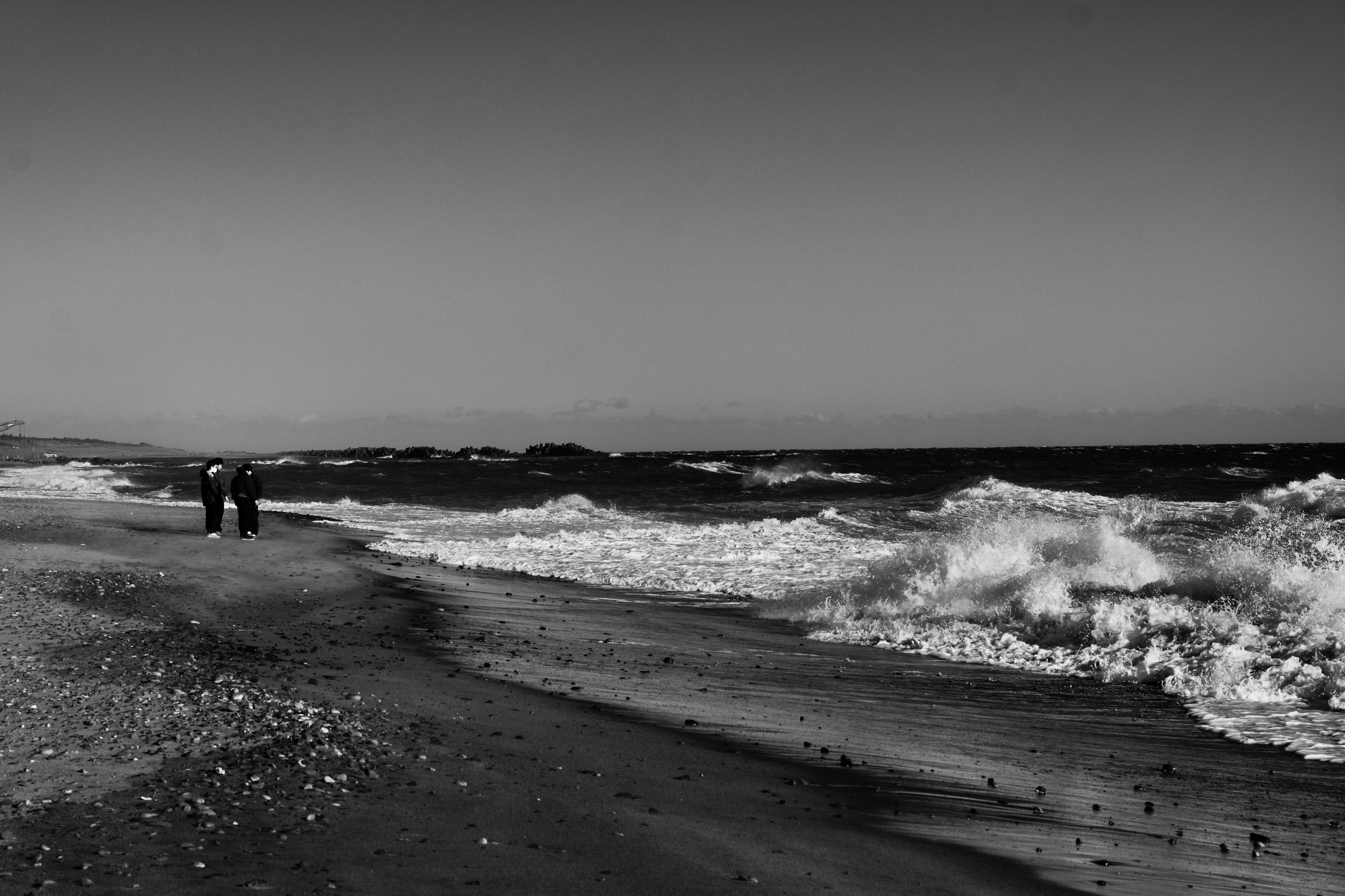 Escena costera en blanco y negro con olas y personas caminando