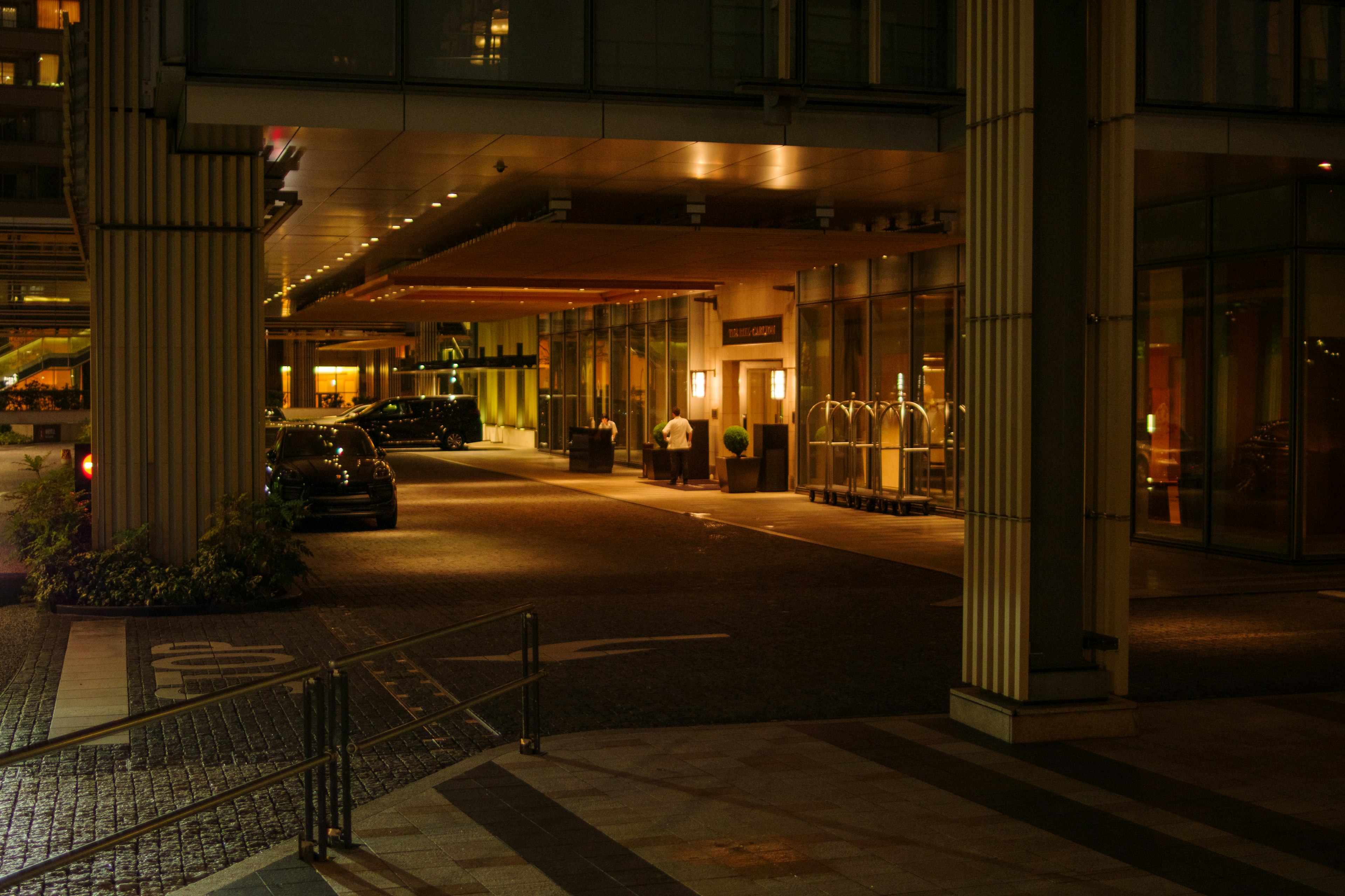 Vista notturna dell'entrata di un hotel di lusso con auto parcheggiate e hall illuminata