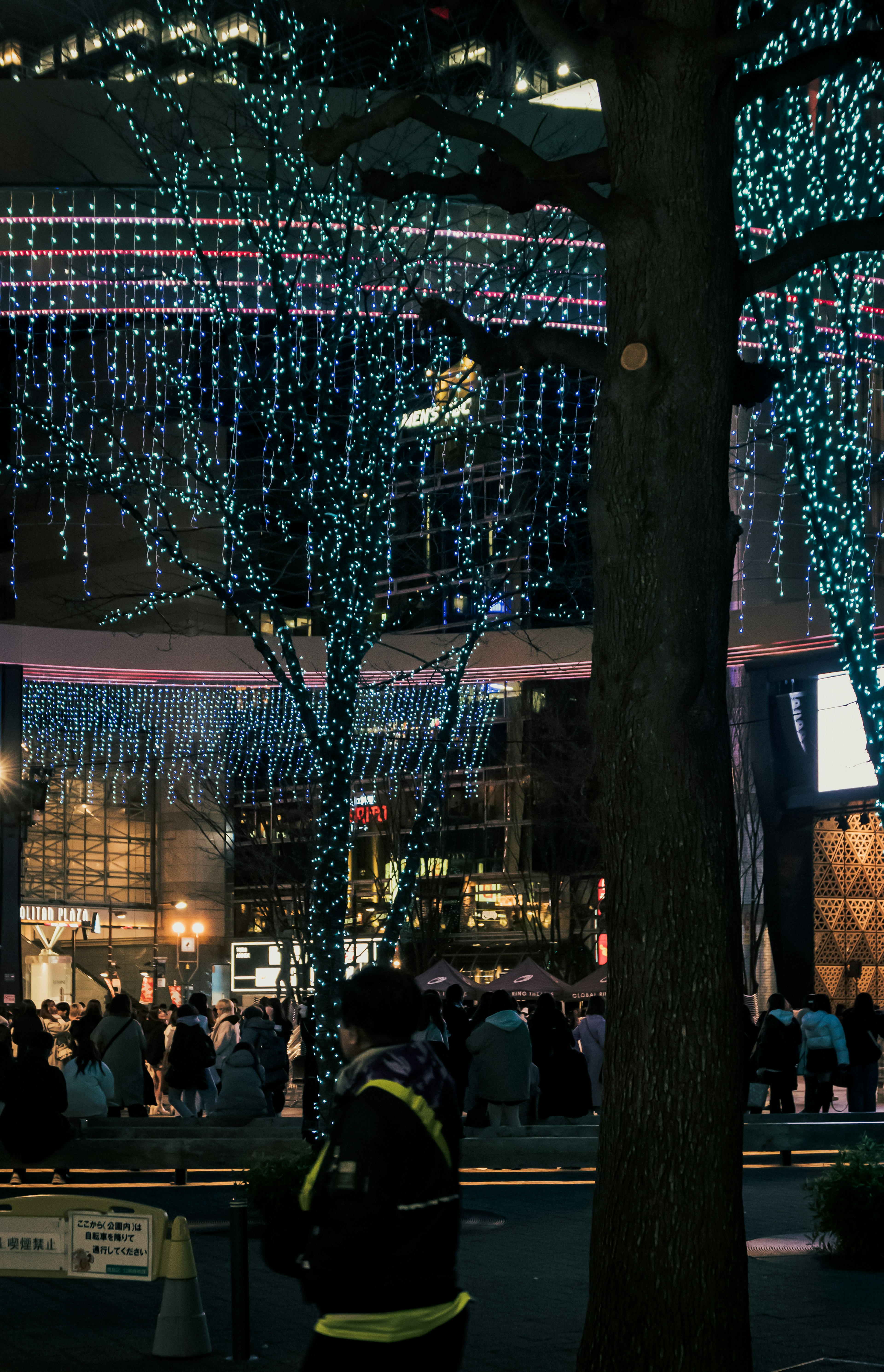 Firefighter standing under blue illuminated trees in a bustling night scene