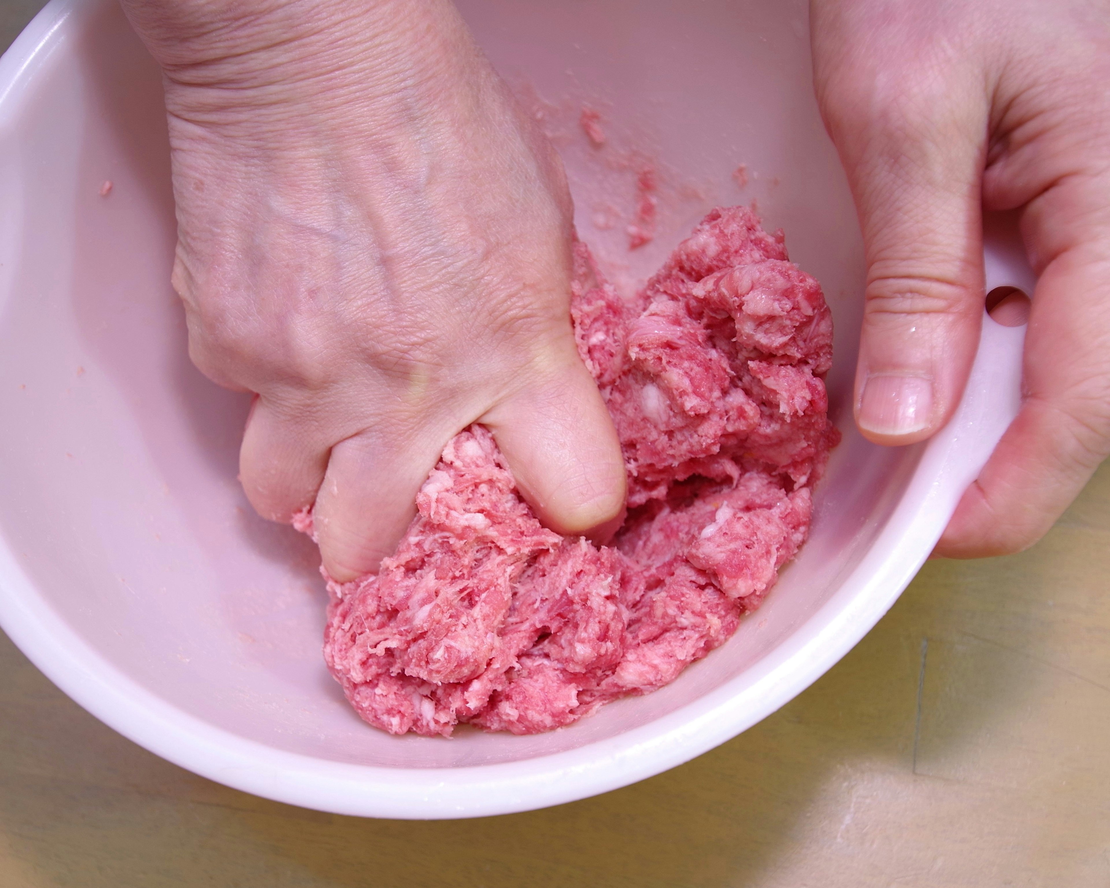 Hands mixing ground meat in a bowl