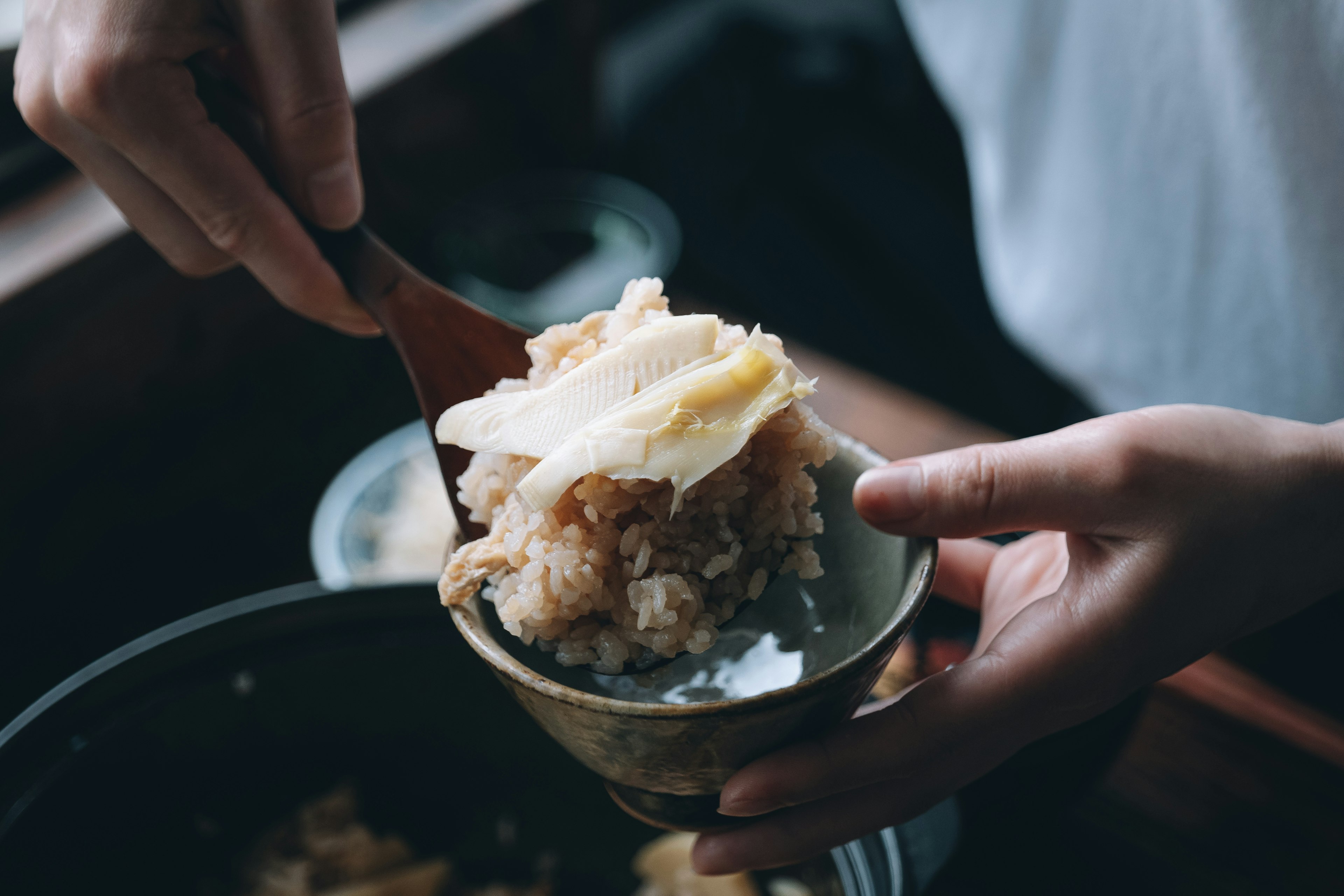 A person serving rice with toppings into a bowl