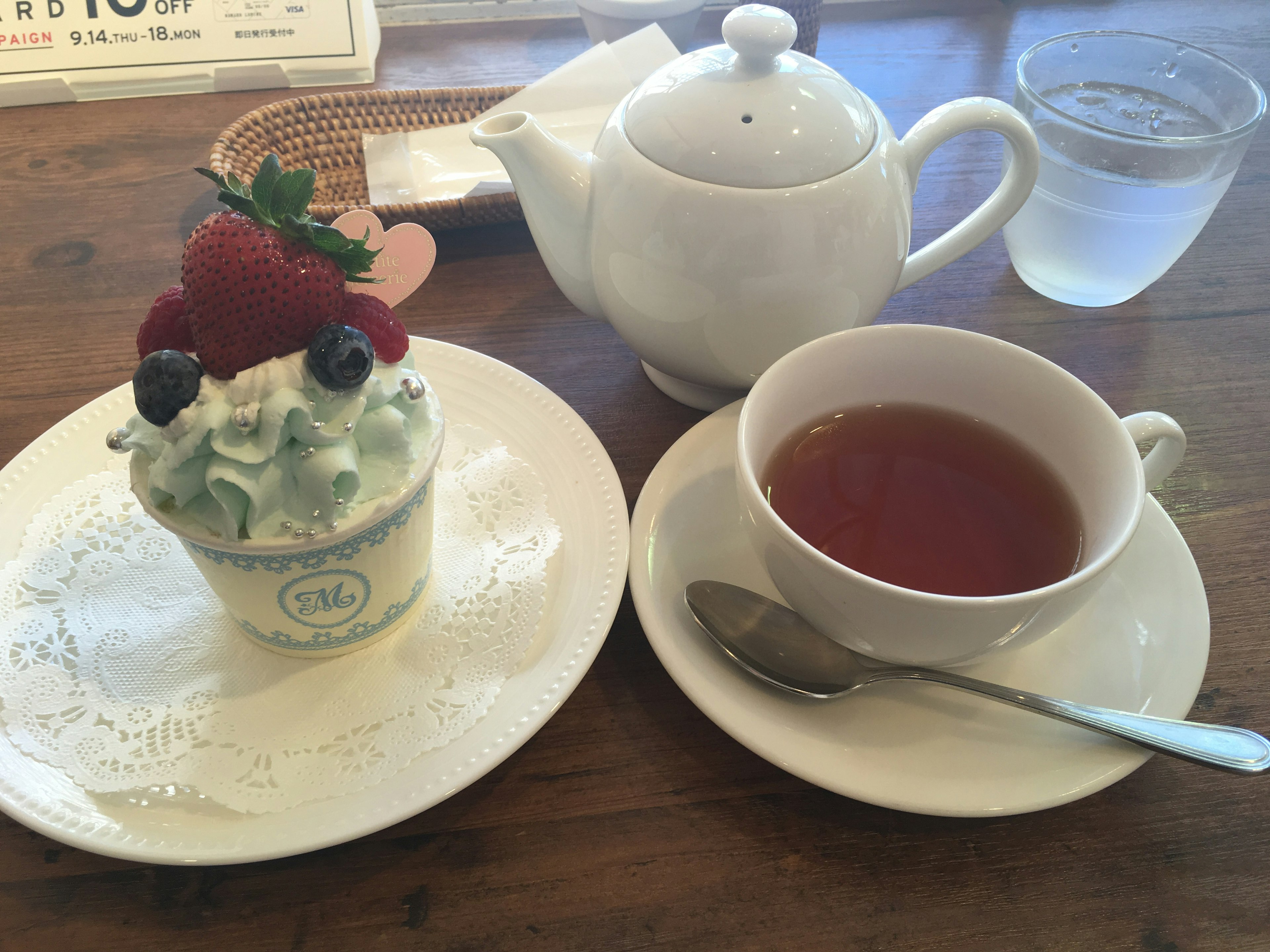 Una tetera blanca y una taza de té sobre una mesa con un postre cubierto de crema y bayas