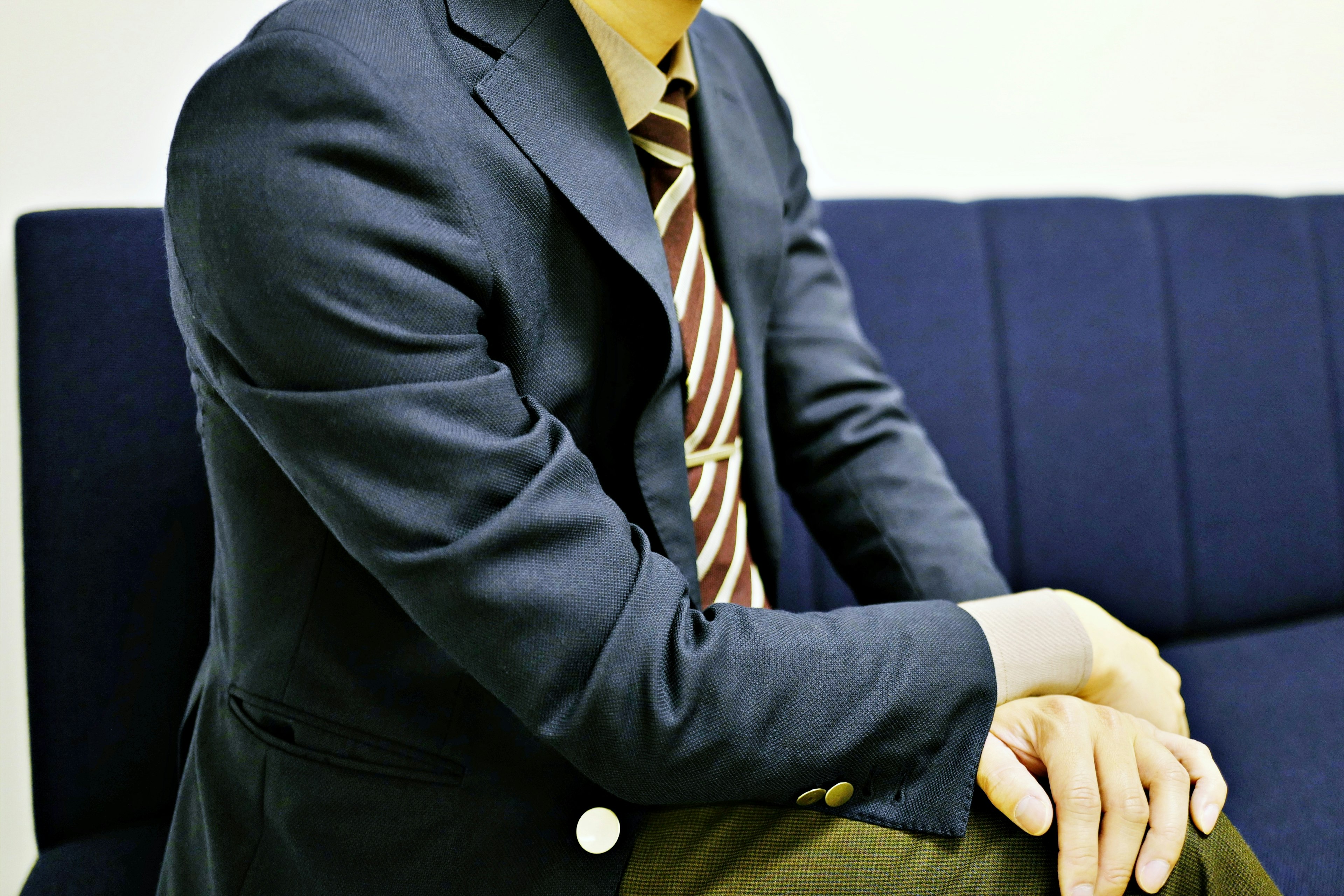 Man in a suit sitting on a blue sofa with arms crossed