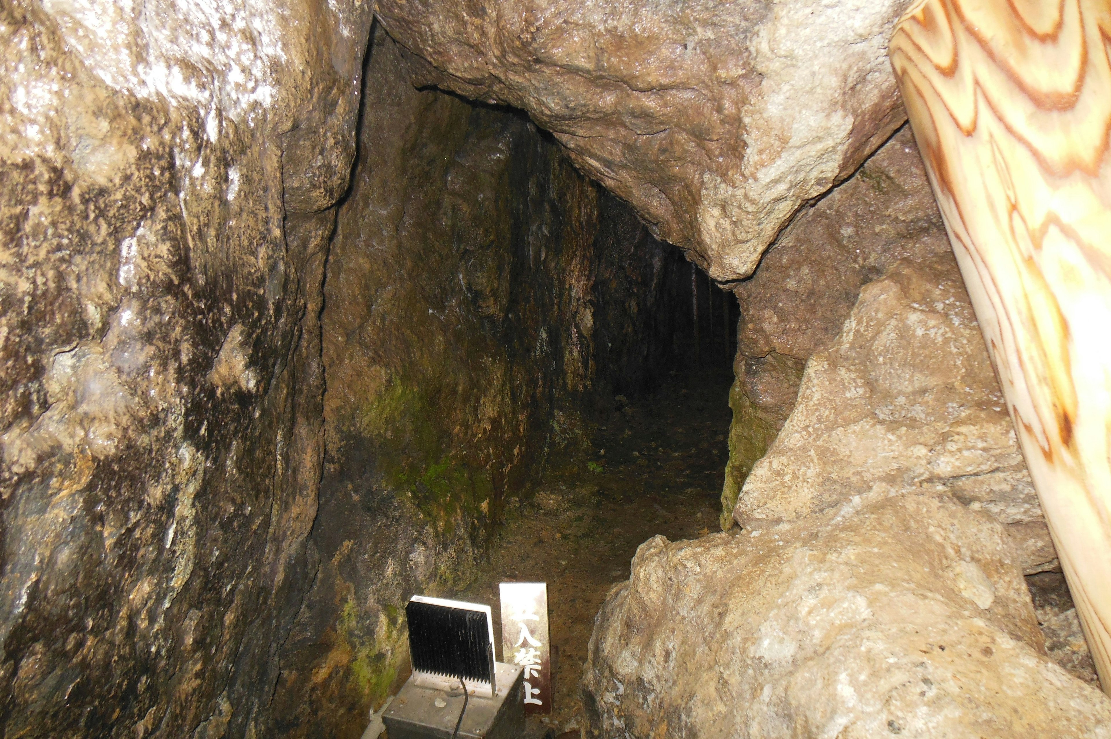 Interior de una cueva estrecha con rocas antiguas y suelo húmedo una computadora está colocada dentro