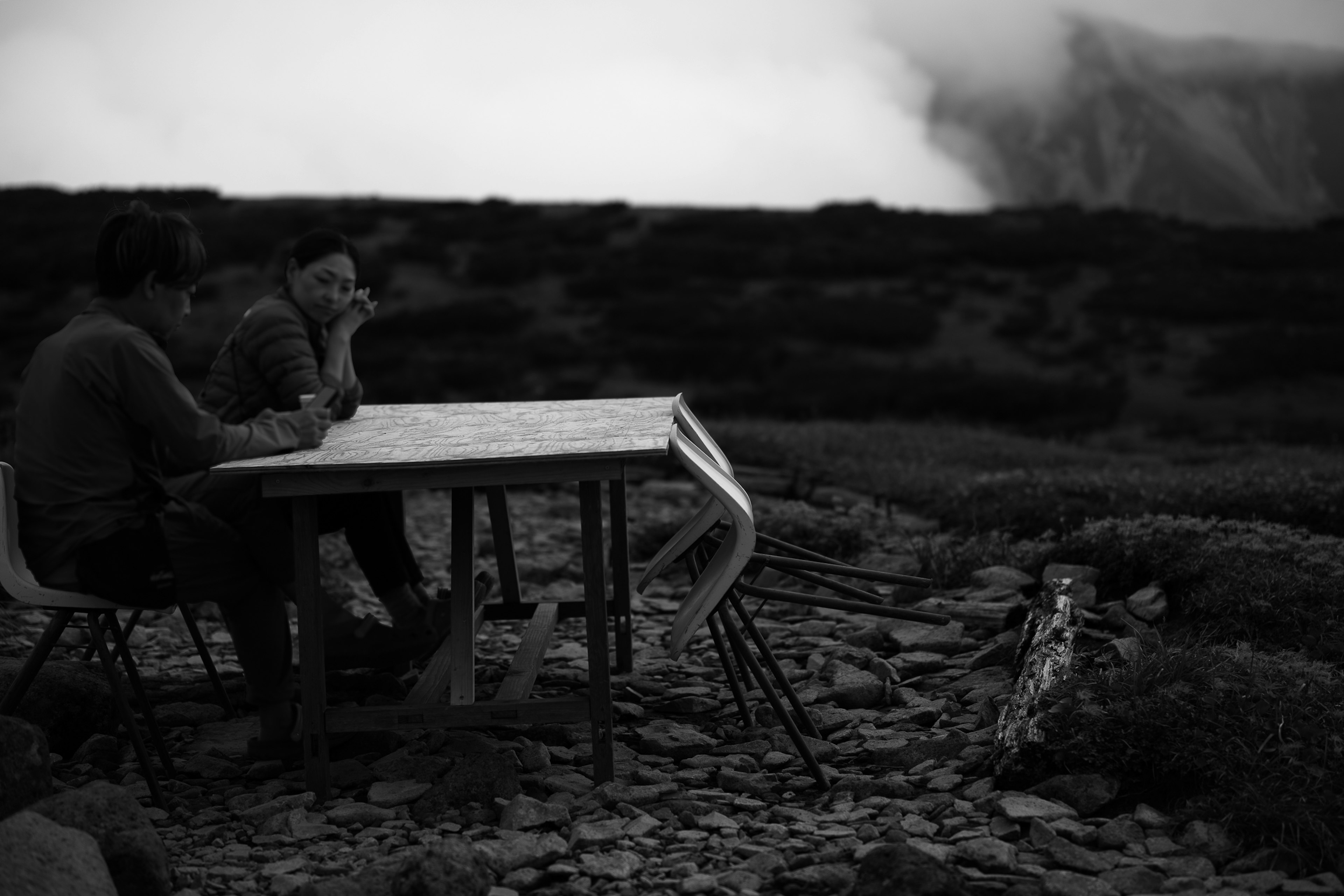 Zwei Personen sitzen an einem Tisch in einer bergigen Landschaft