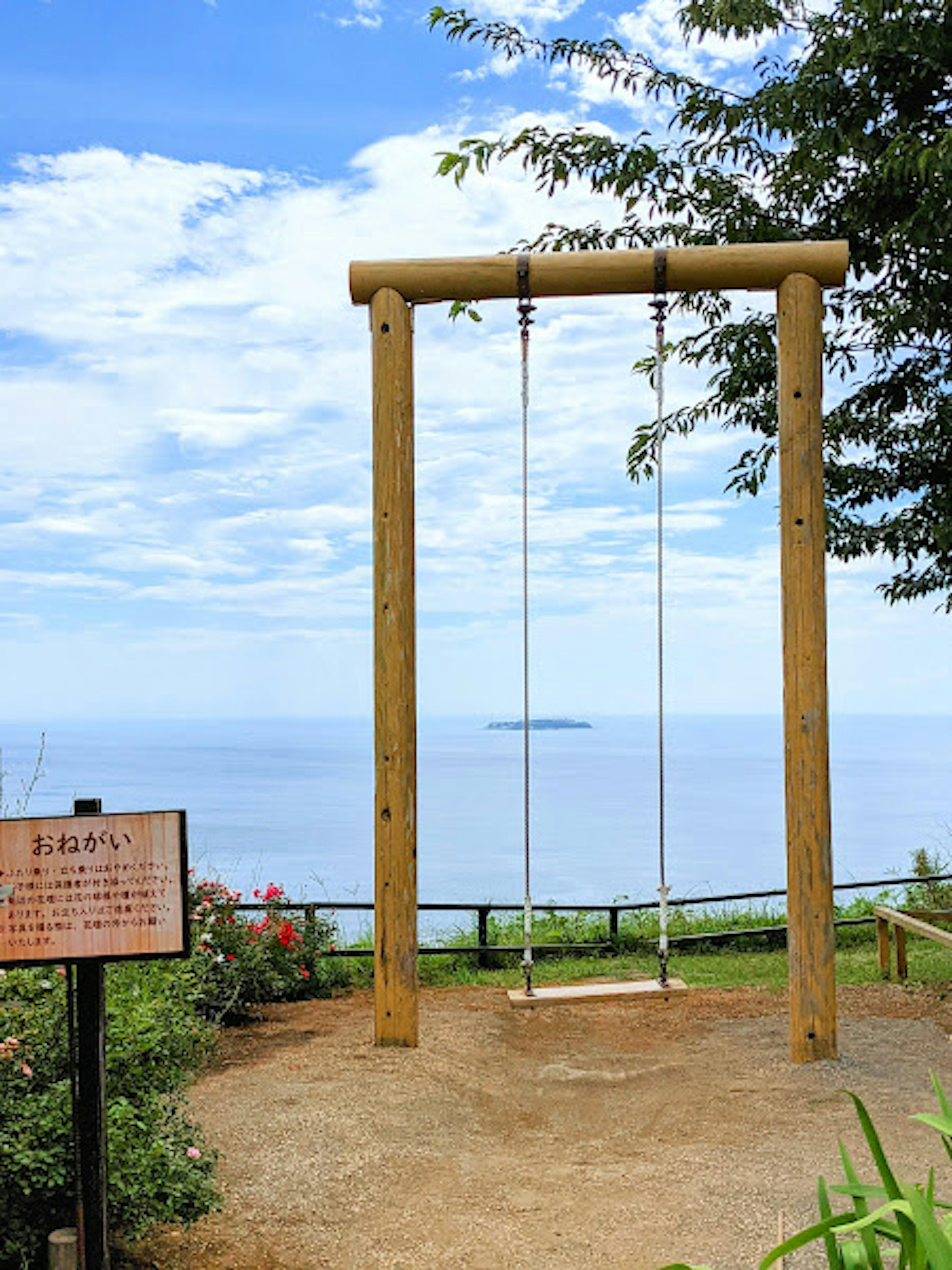 青い空と海を背景にした木製のブランコと案内板