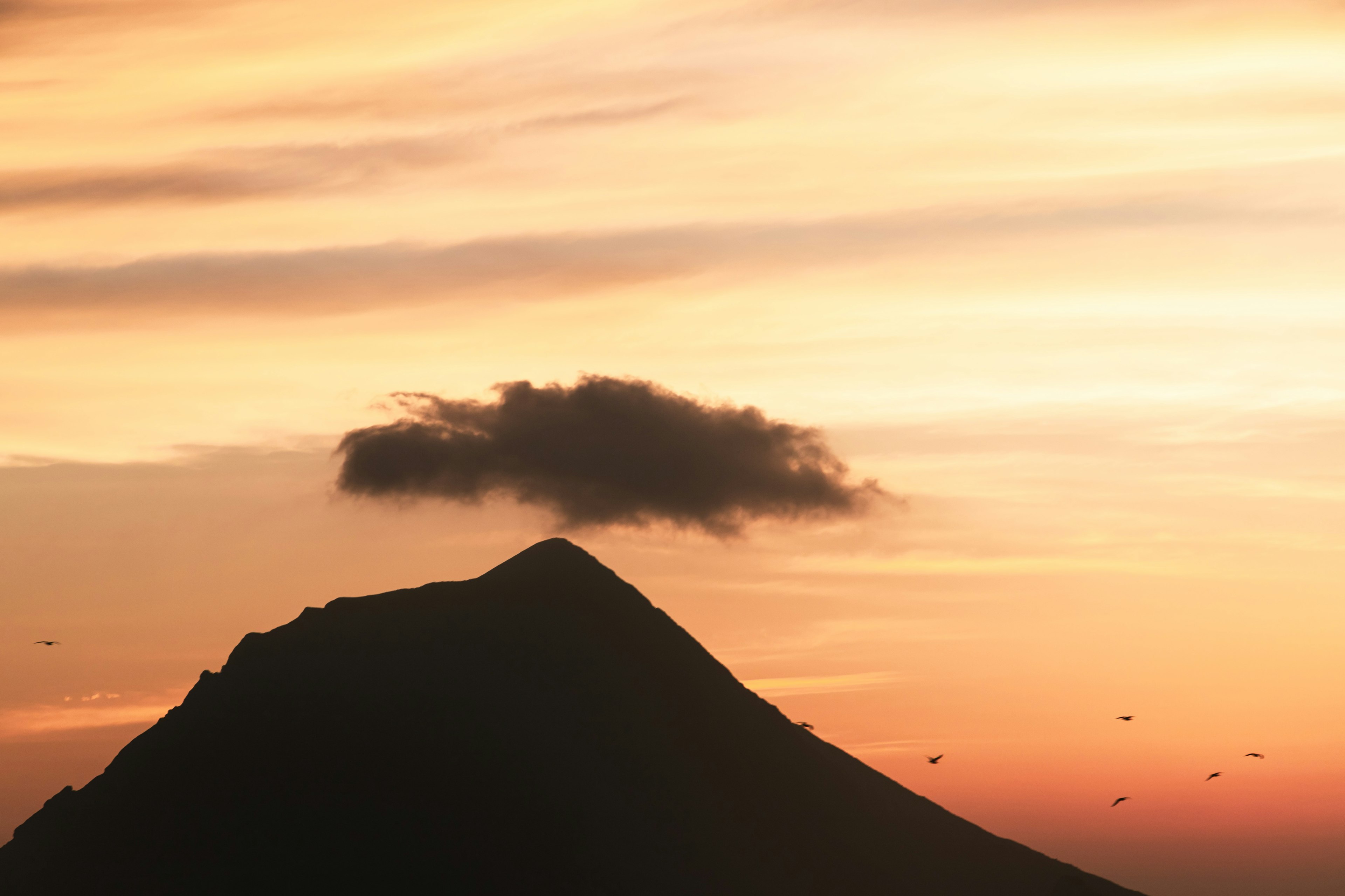 Silueta de una montaña con una nube contra un cielo de atardecer