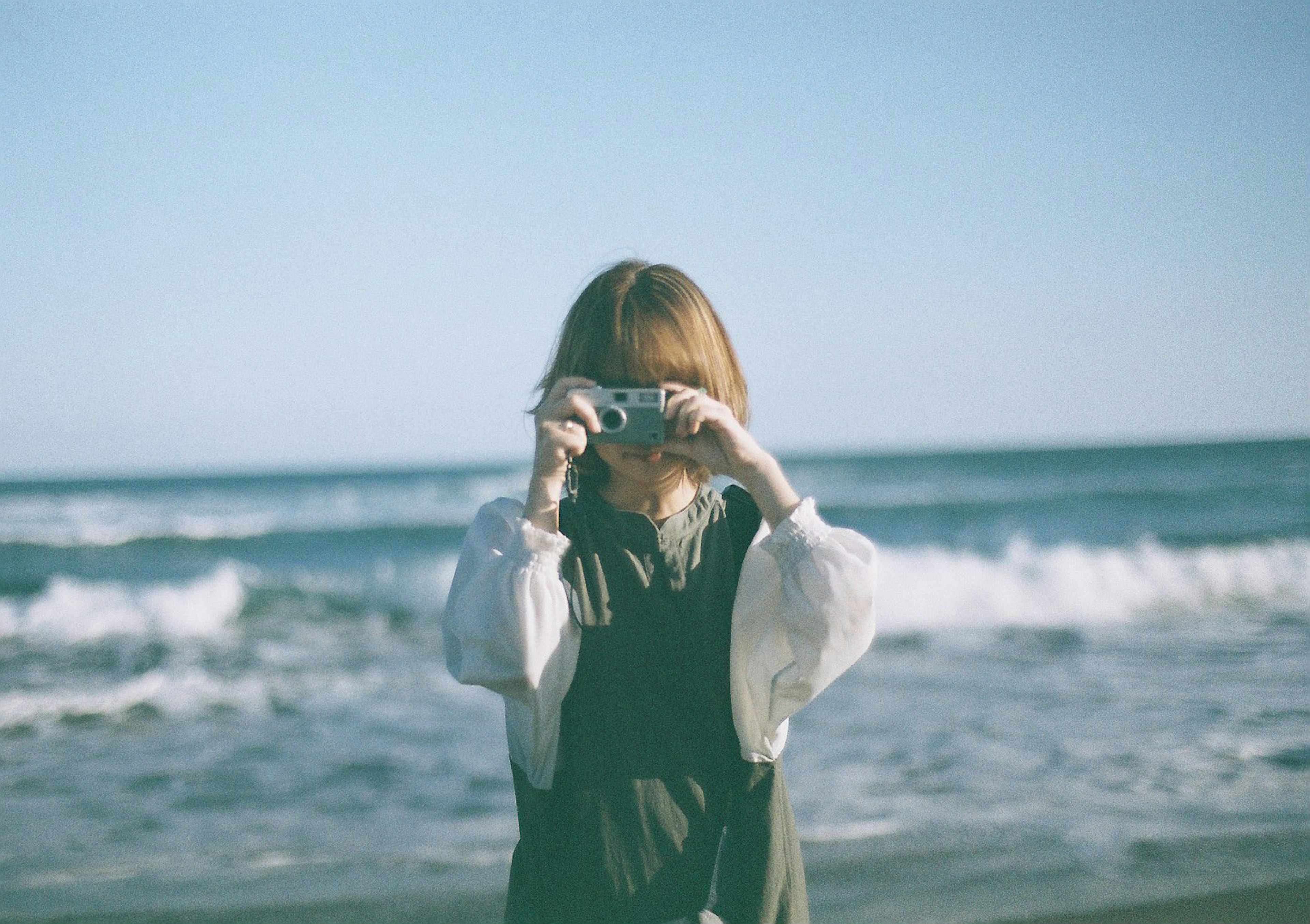 Une femme tenant un appareil photo à la plage avec un ciel bleu et des vagues en arrière-plan