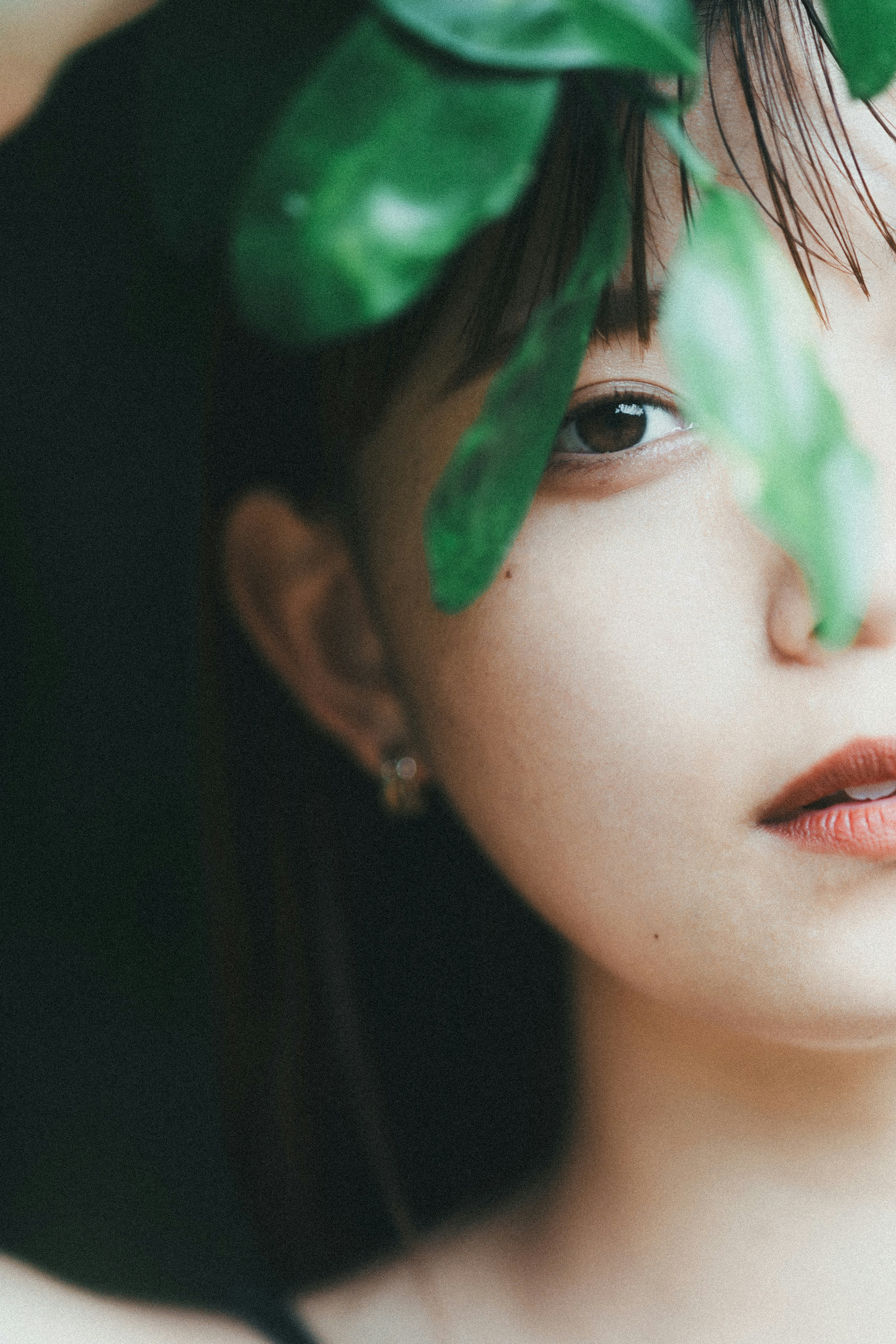 Close-up portrait of a woman partially hidden by green leaves