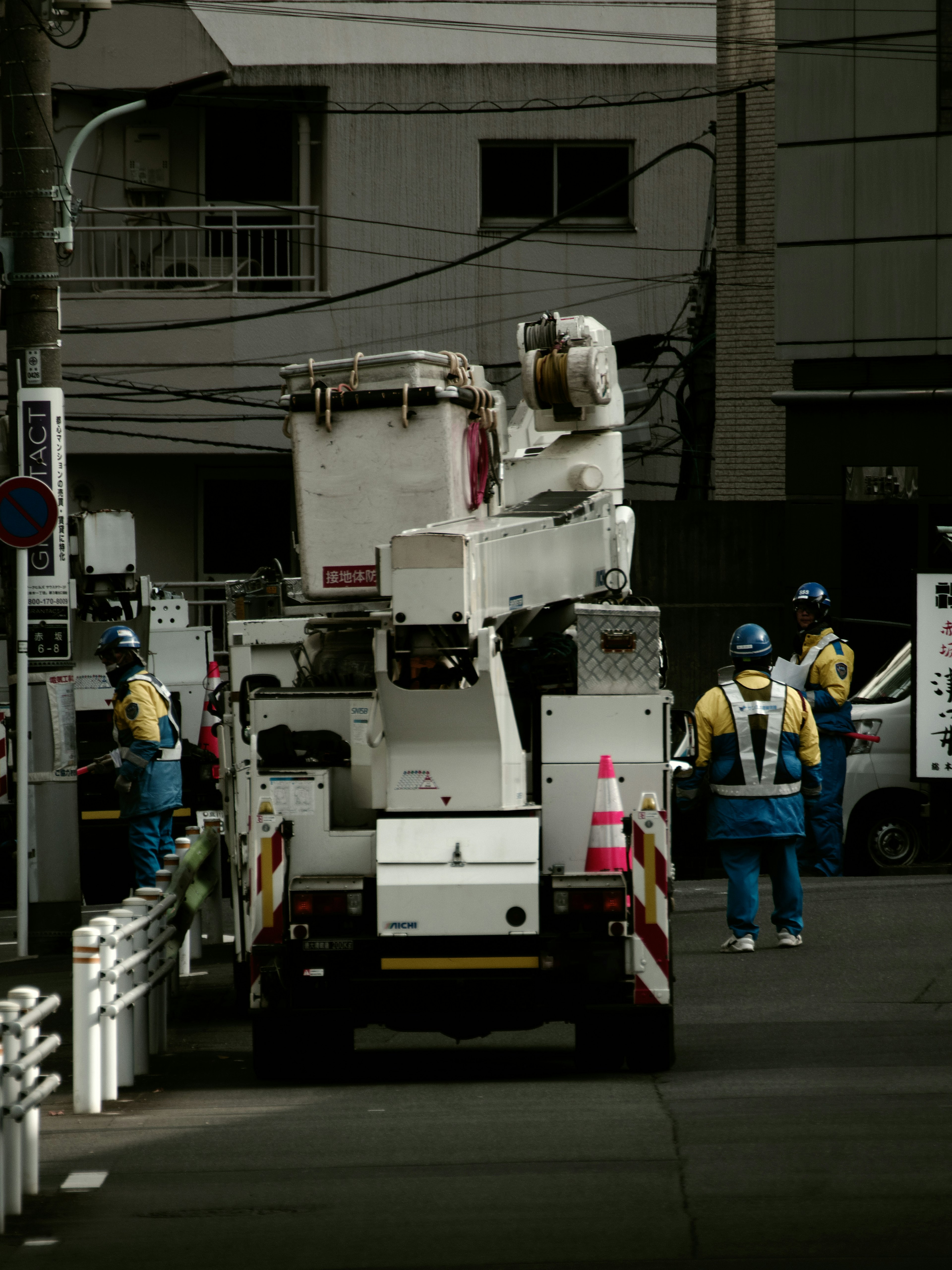 作業用のクレーン車と作業員が写っている街中の風景