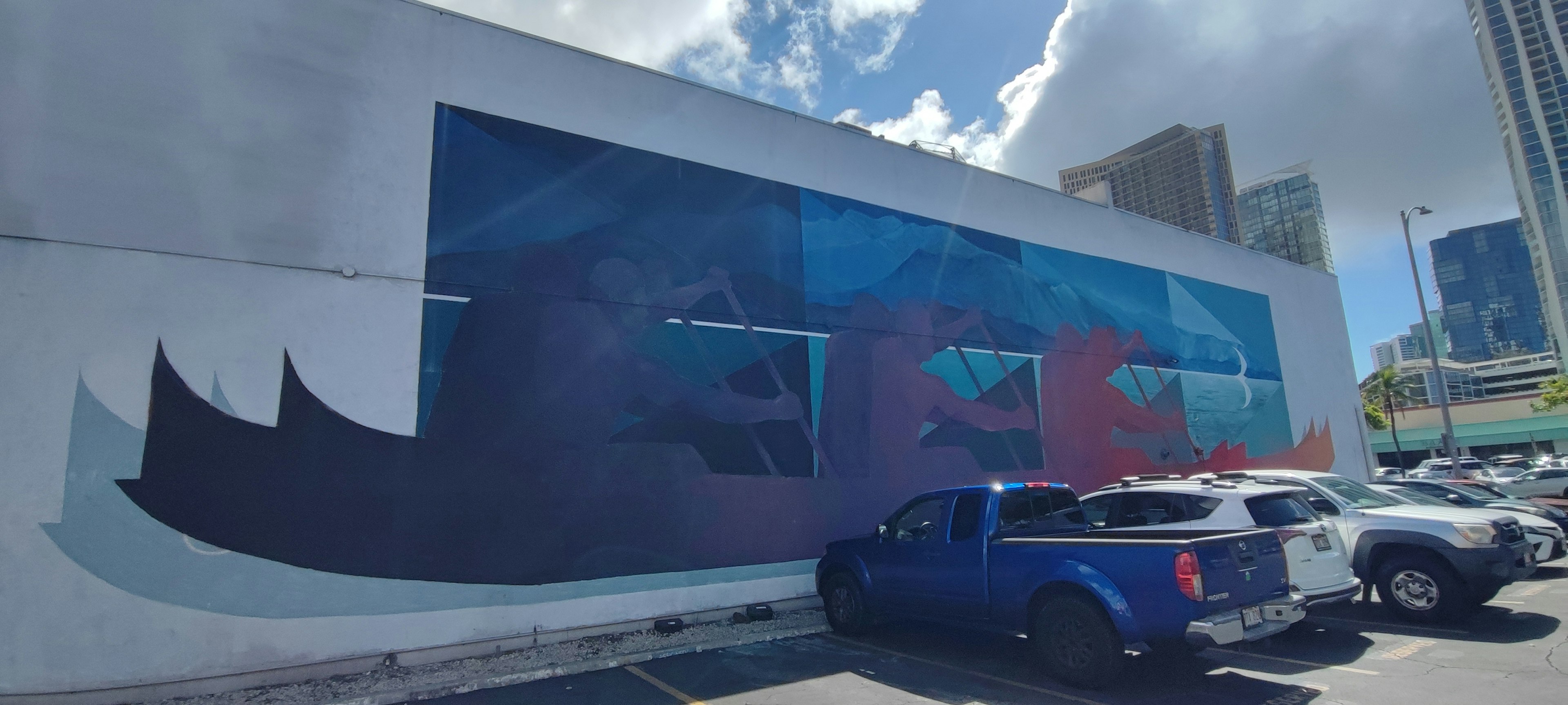 Escena de estacionamiento con un coche azul y un gran mural