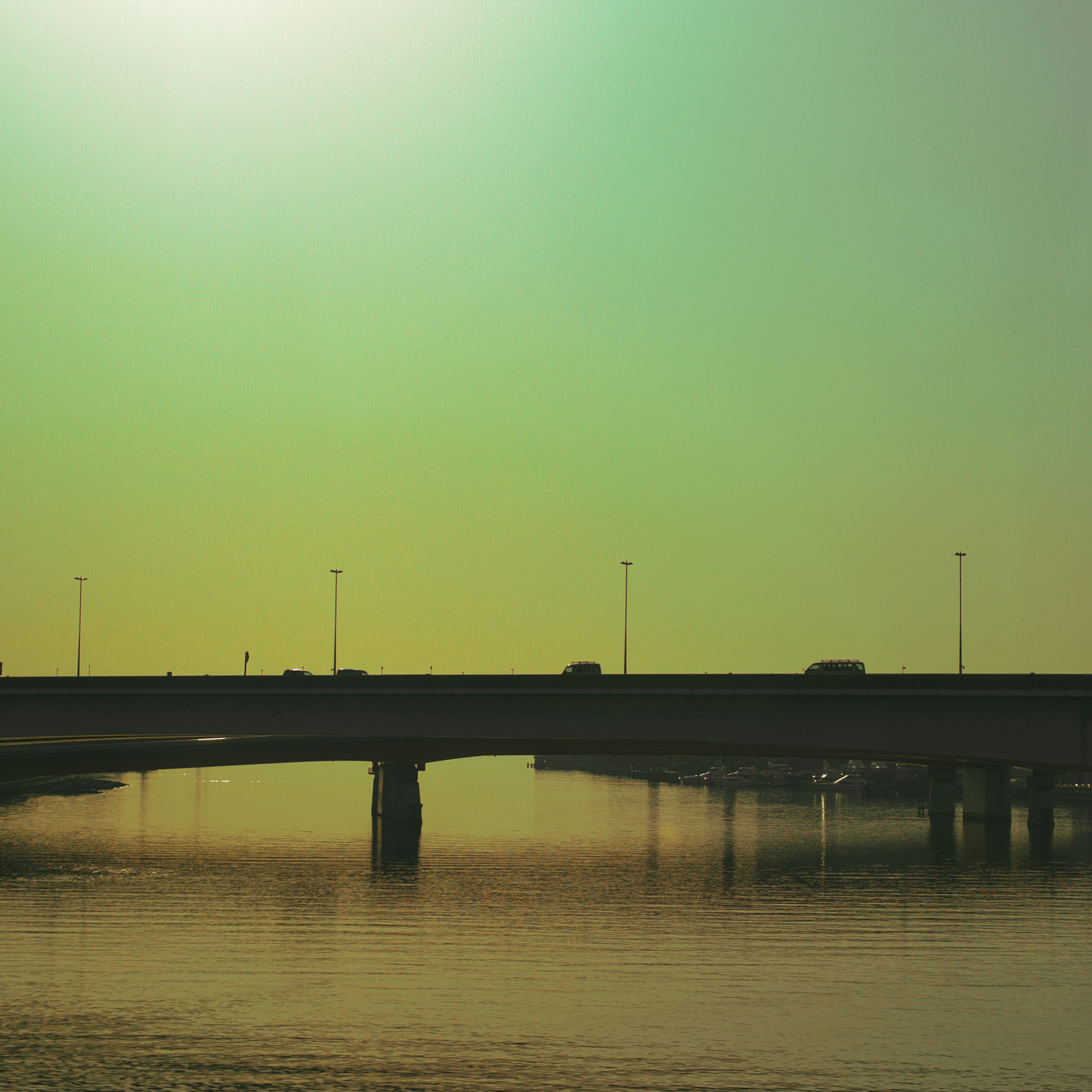 Puente silueteado contra un cielo verdoso con reflejos en el agua