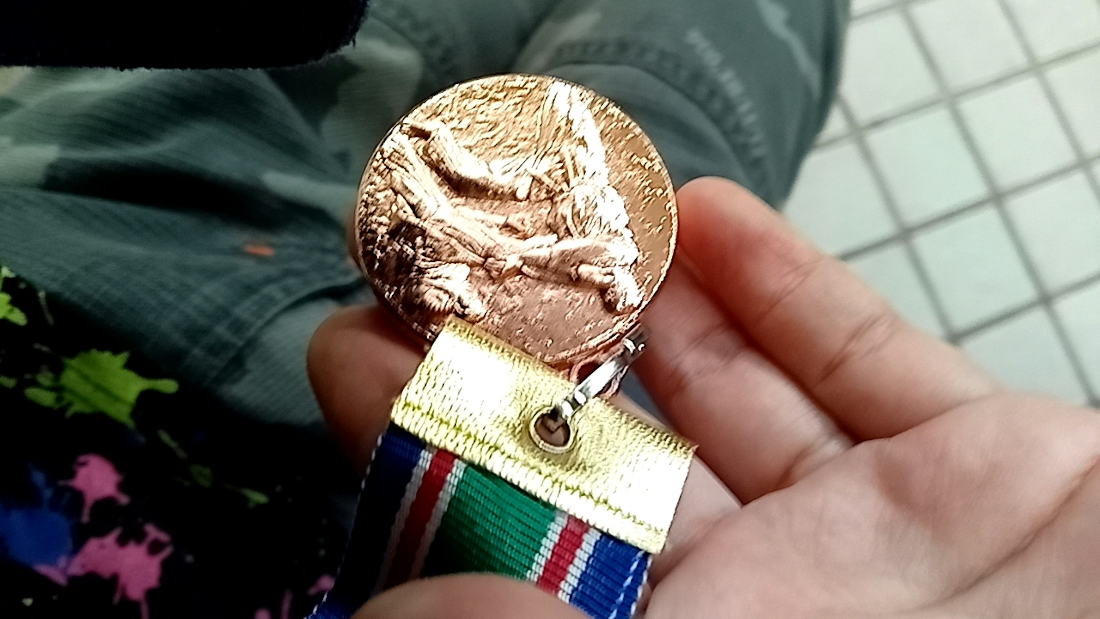 Close-up of a bronze medal held in hand with colorful ribbon