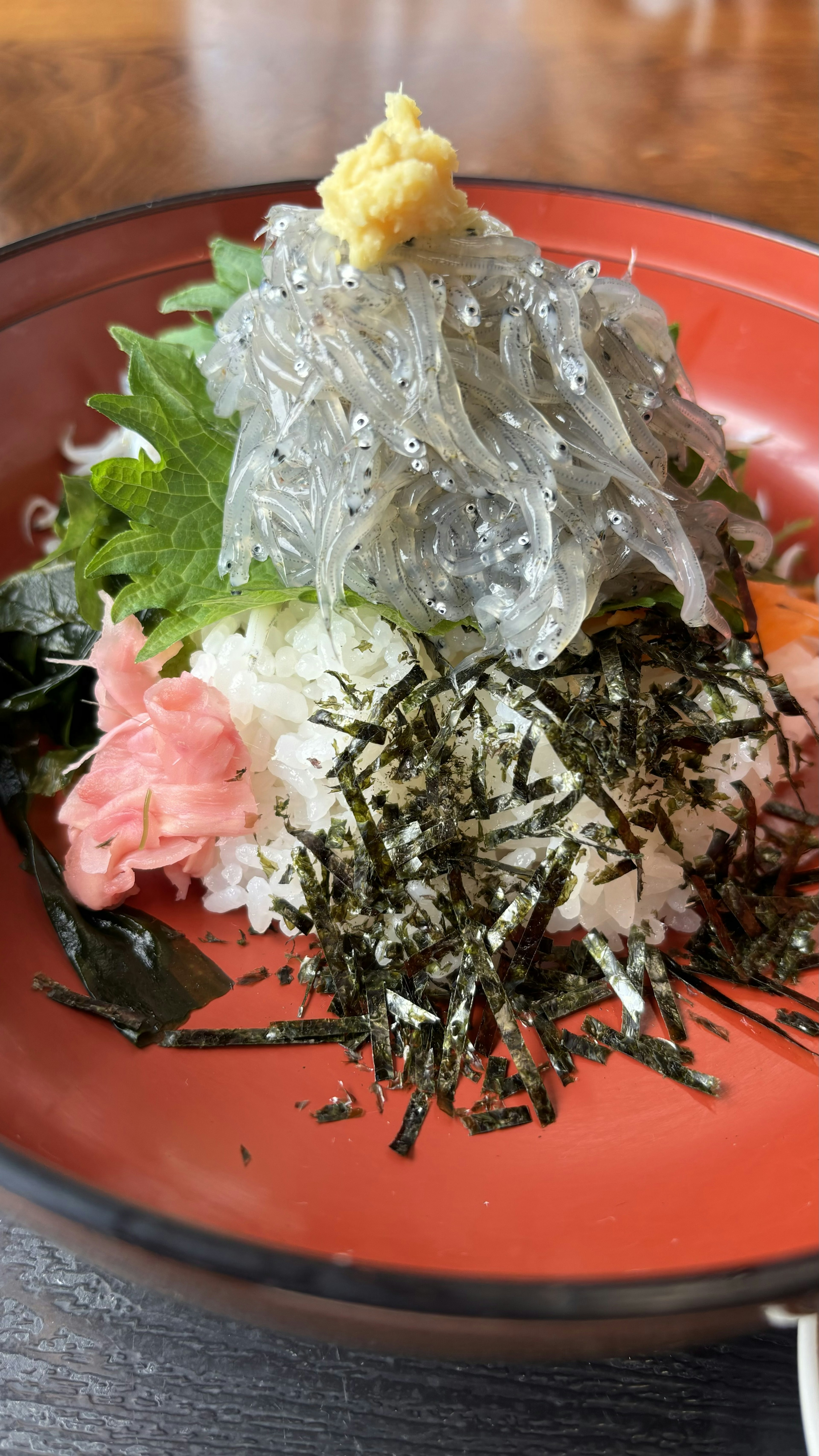 A colorful dish featuring fresh sashimi and seaweed on a red plate