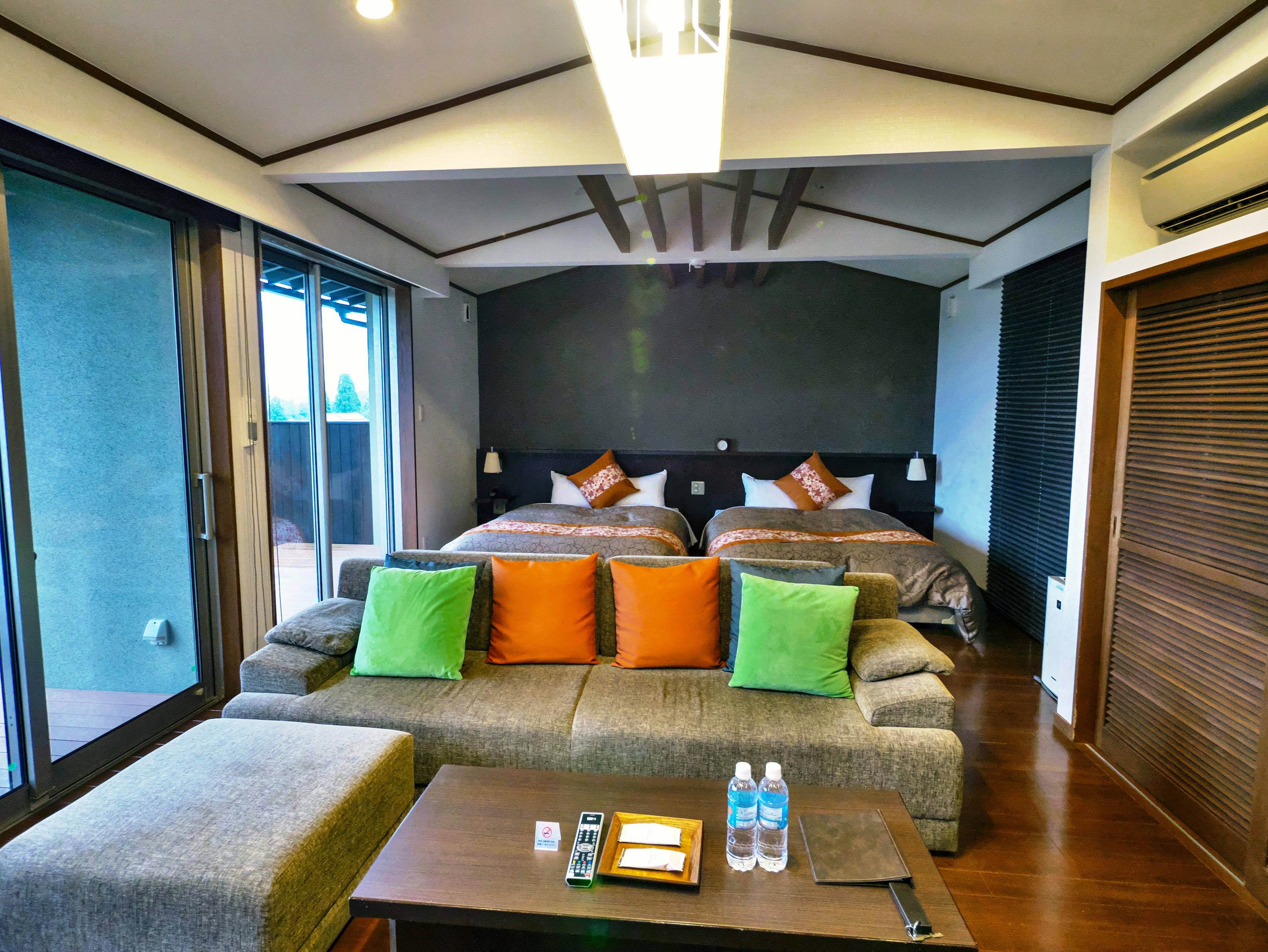 Modern hotel room design with green and orange cushions on the sofa two beds in the background