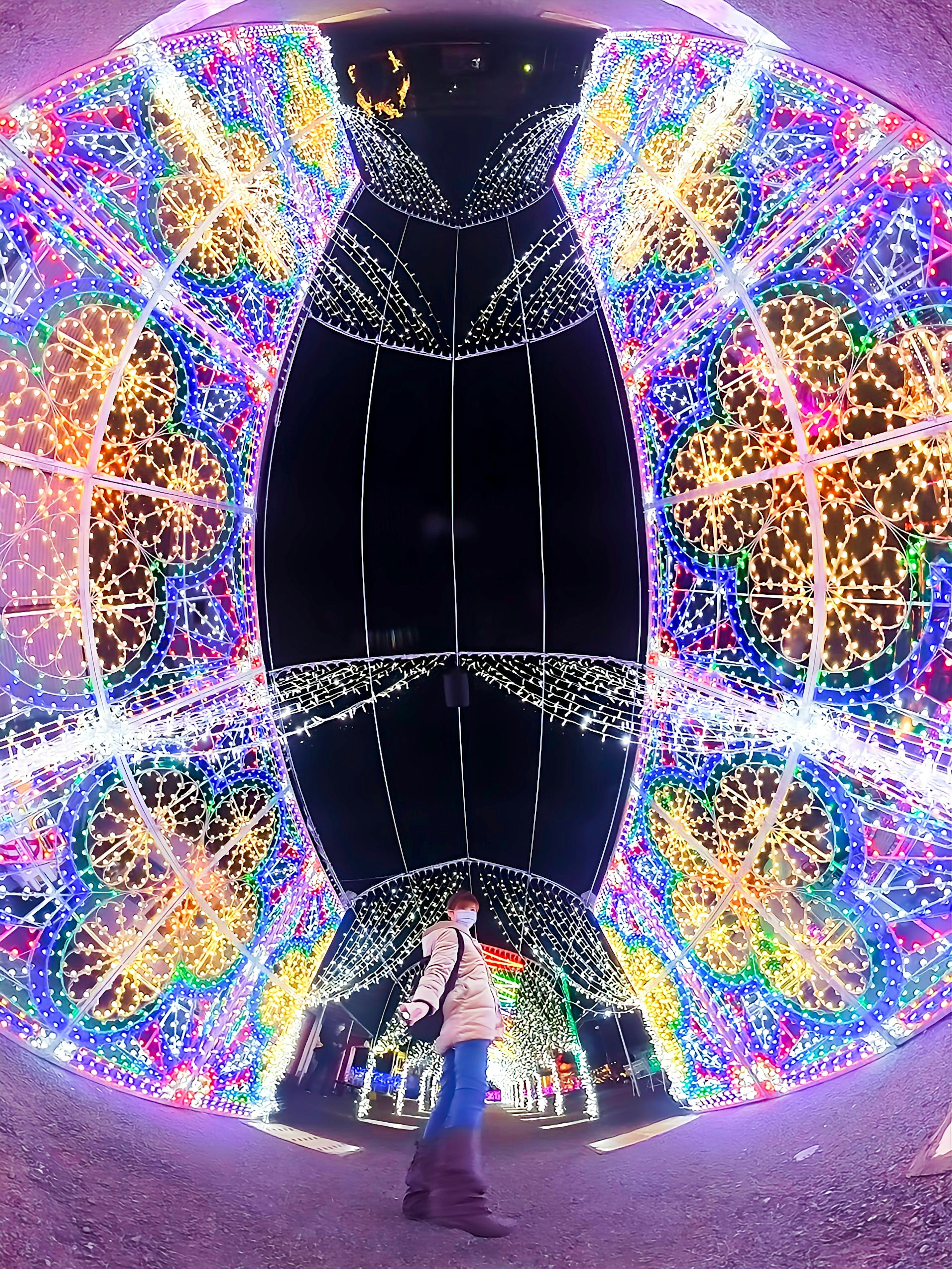 A person walking through a brightly lit tunnel decorated with colorful lights