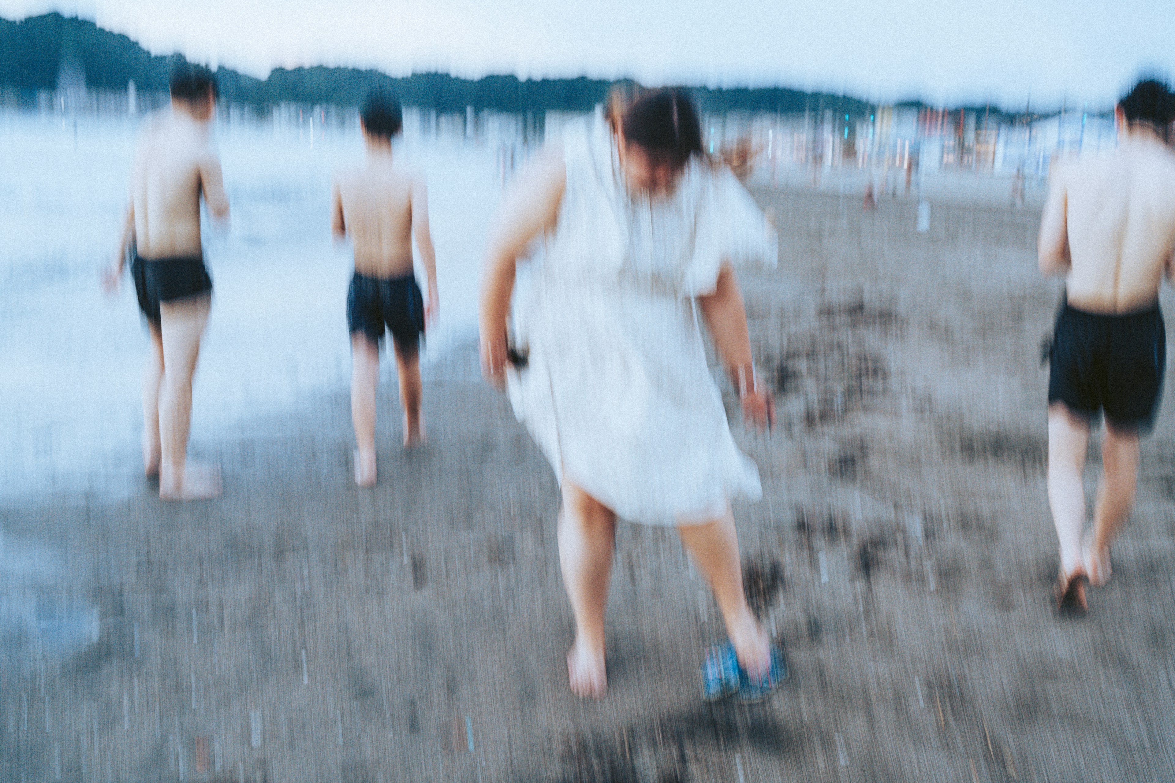 A woman in a white dress walking on the beach with several men in the background