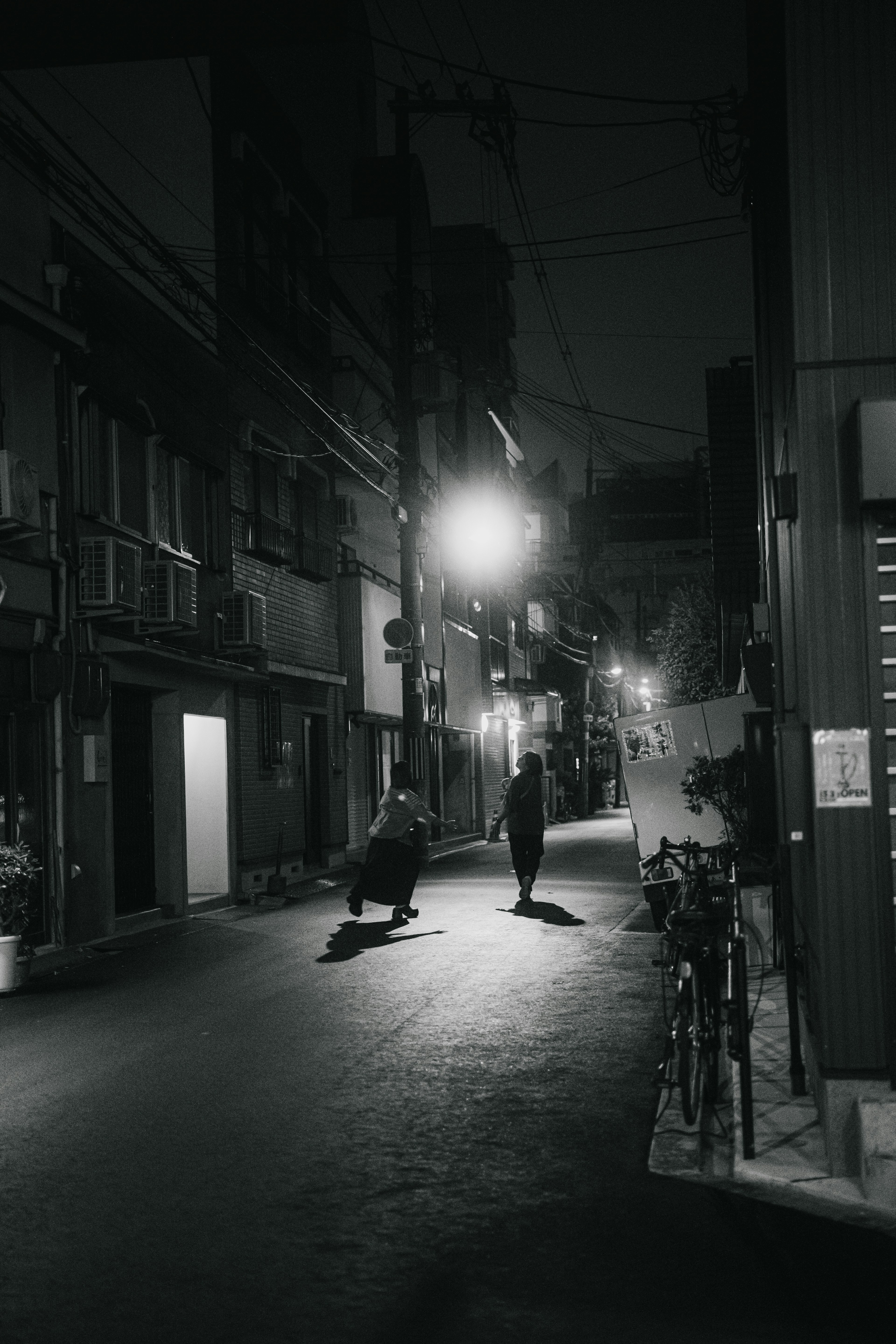 Dos figuras de pie en un callejón tranquilo por la noche con una farola