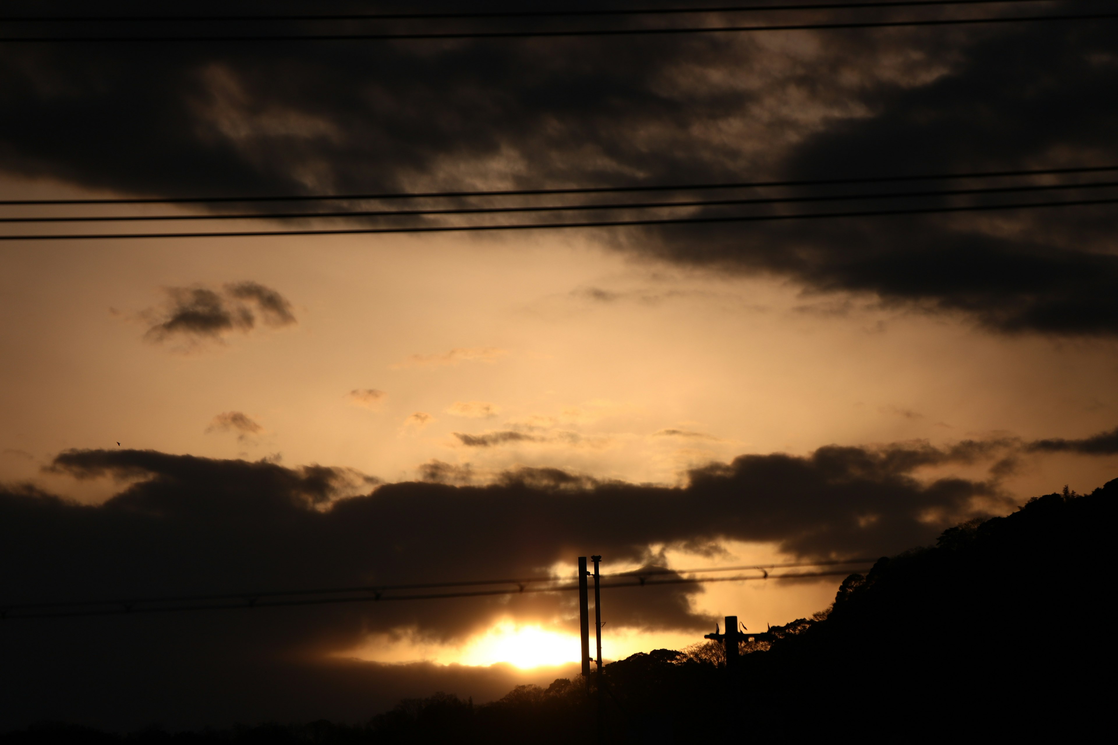 Silueta de atardecer con nubes oscuras rodeando postes eléctricos