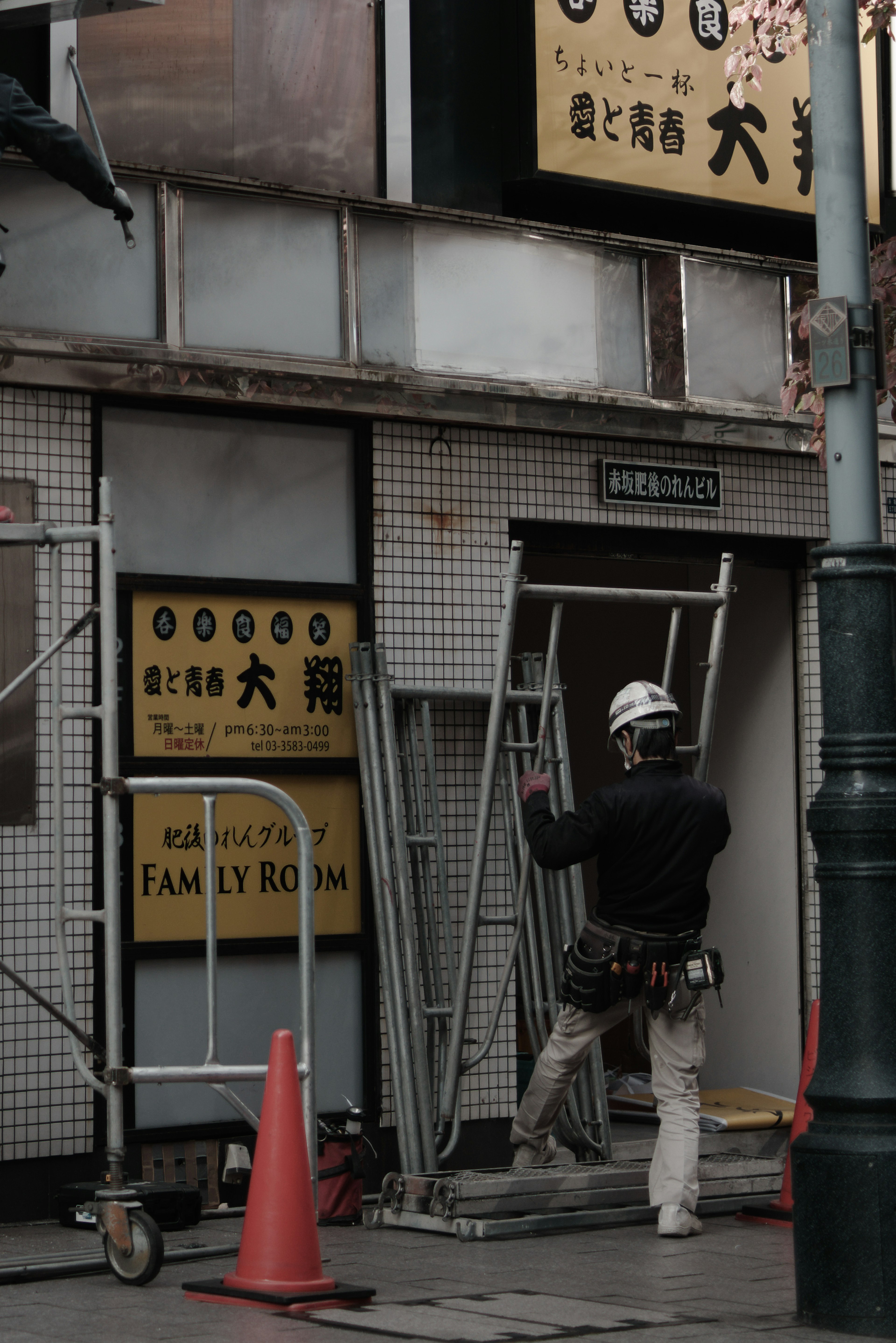 作業員が階段を持っている工事現場の写真 工事用の看板やオレンジのコーンが見える