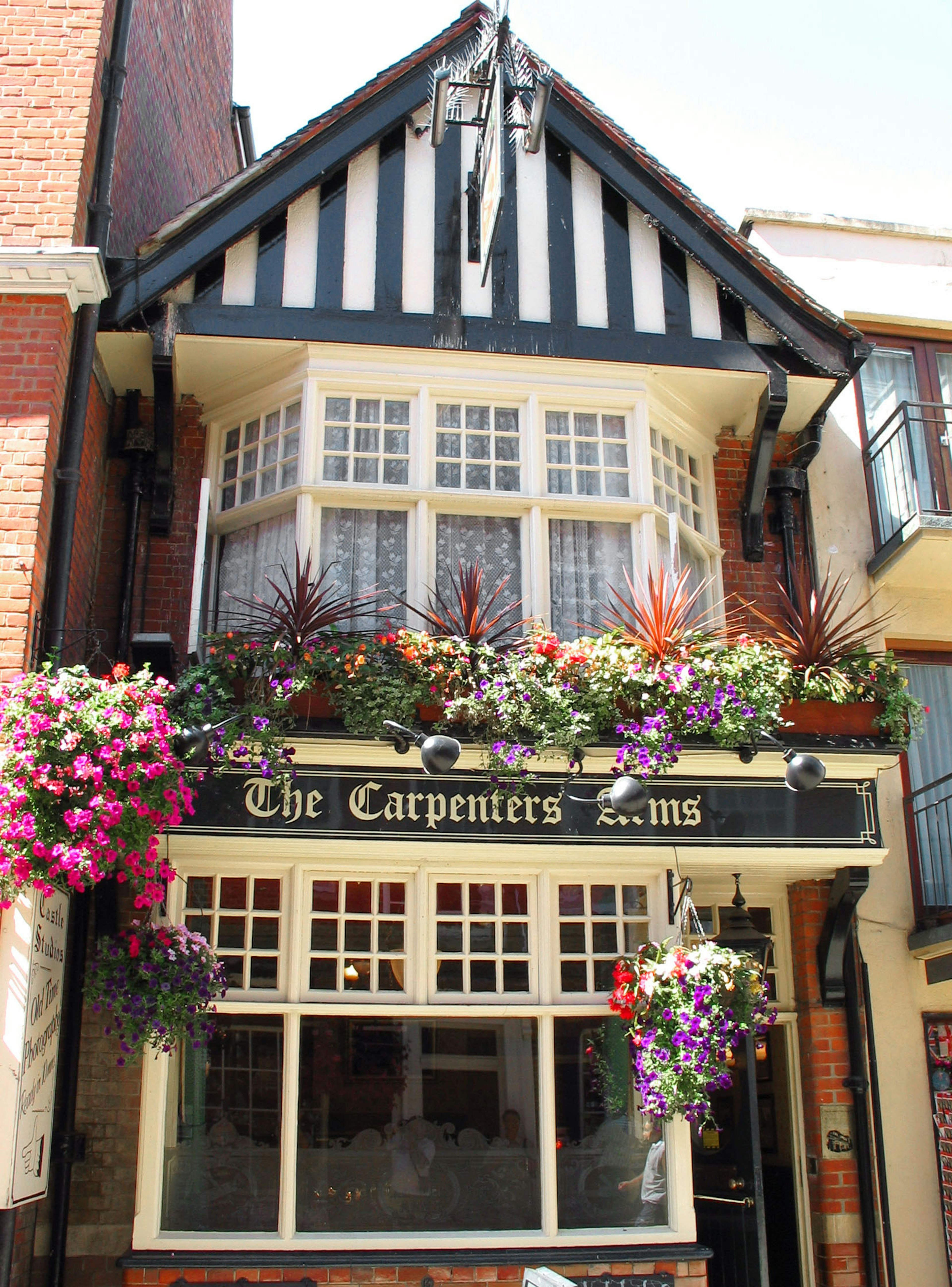 Der Pub Carpenters Arms mit einer schwarz-weißen gestreiften Fassade, geschmückt mit bunten Blumen