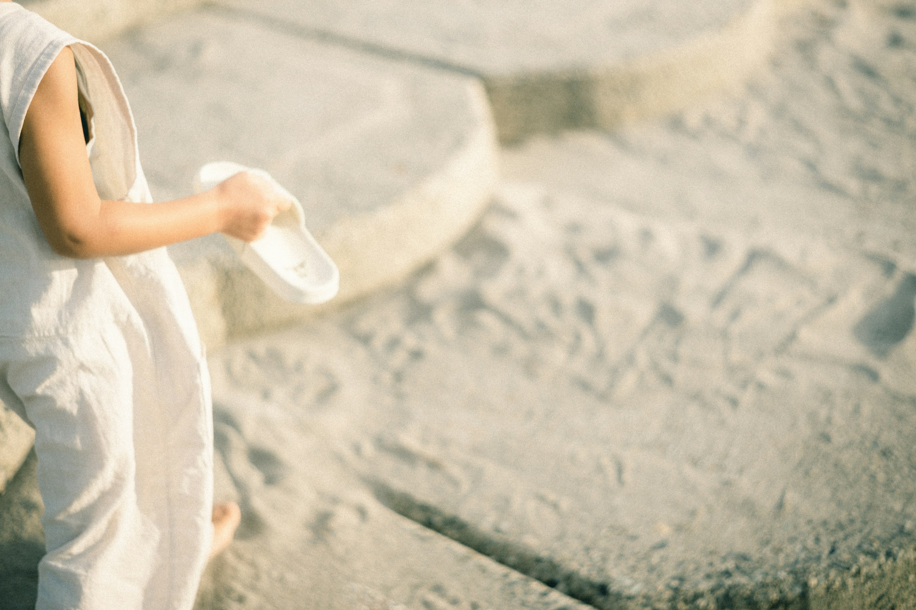 Child wearing white clothing walking on sand