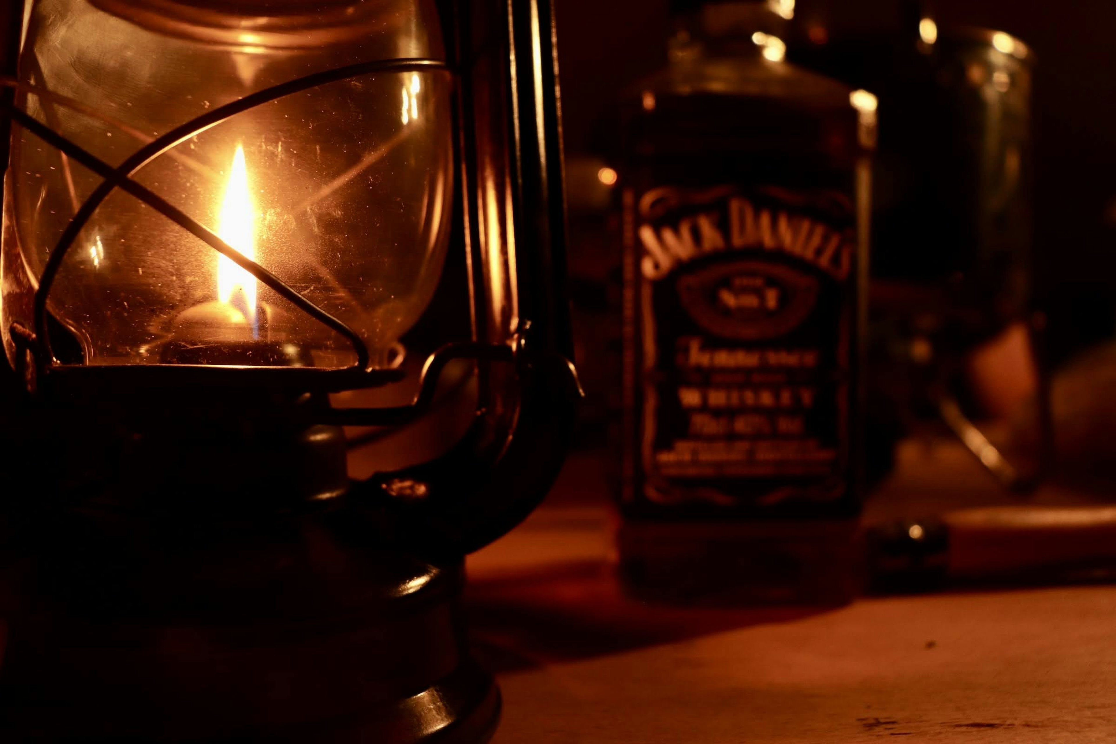 Kedekatan lampu minyak dan botol Jack Daniel's di latar belakang gelap