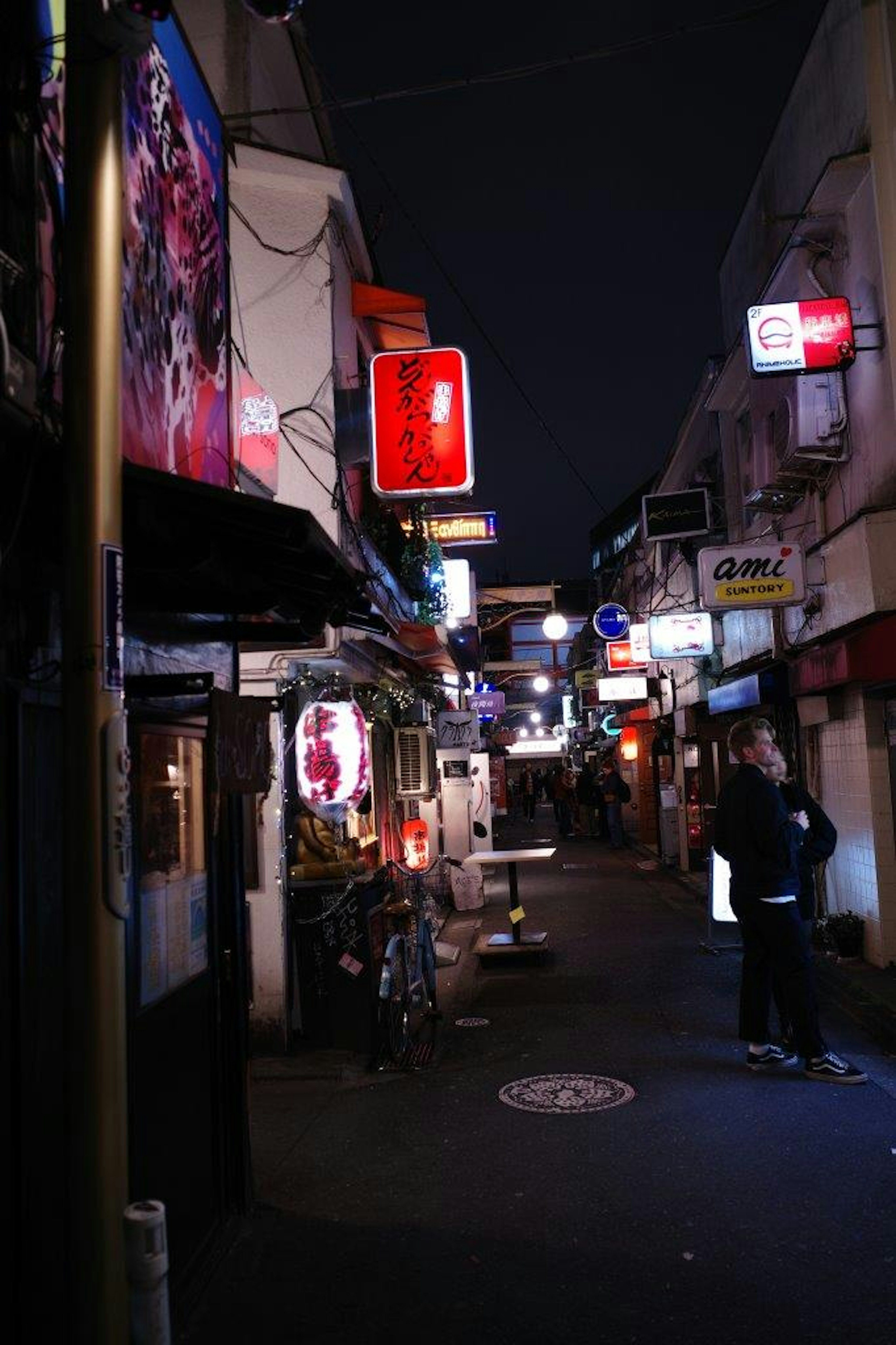 Escena de una calle estrecha de noche con letreros de neón y tiendas