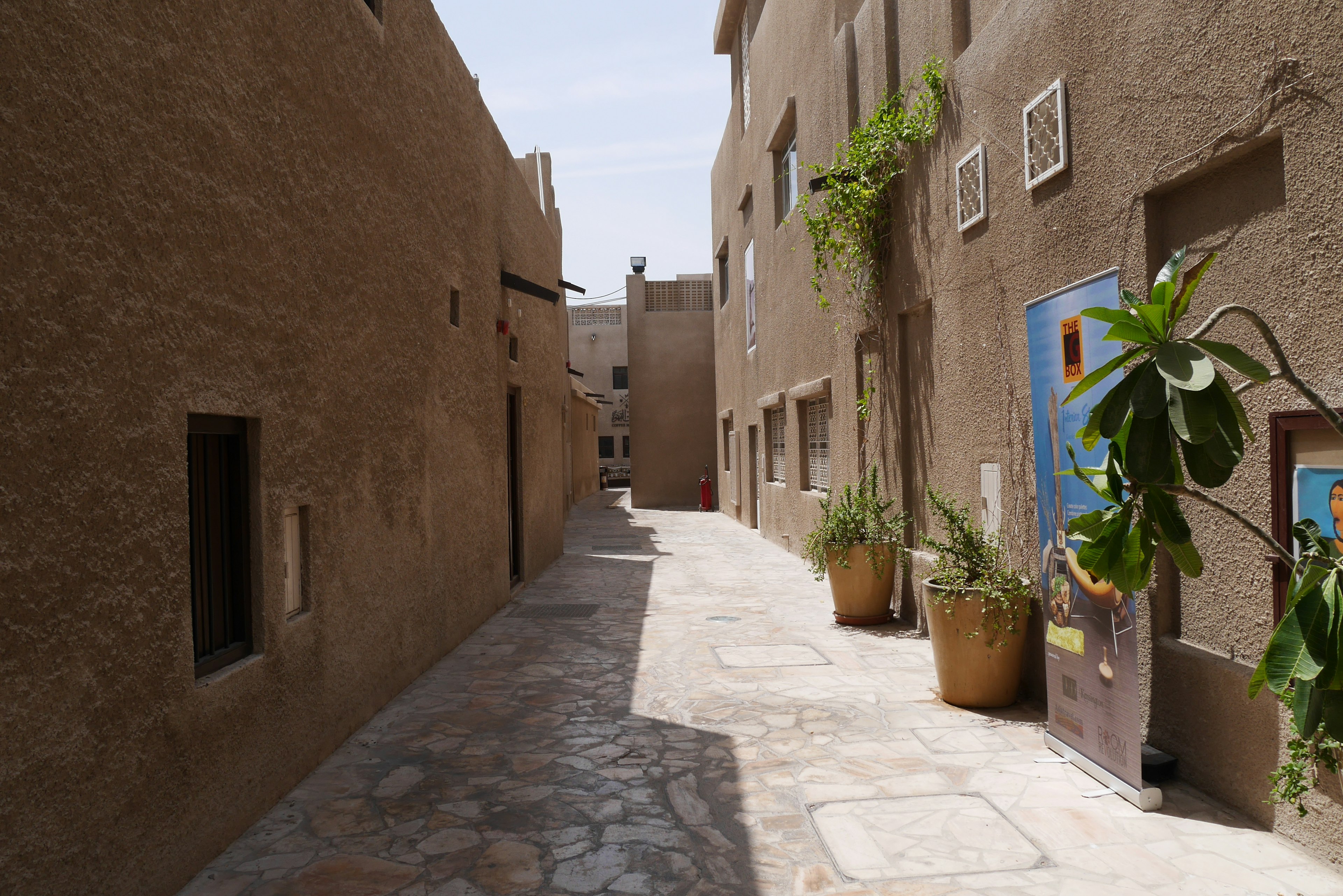 Callejón estrecho con edificios de color arena y plantas en macetas