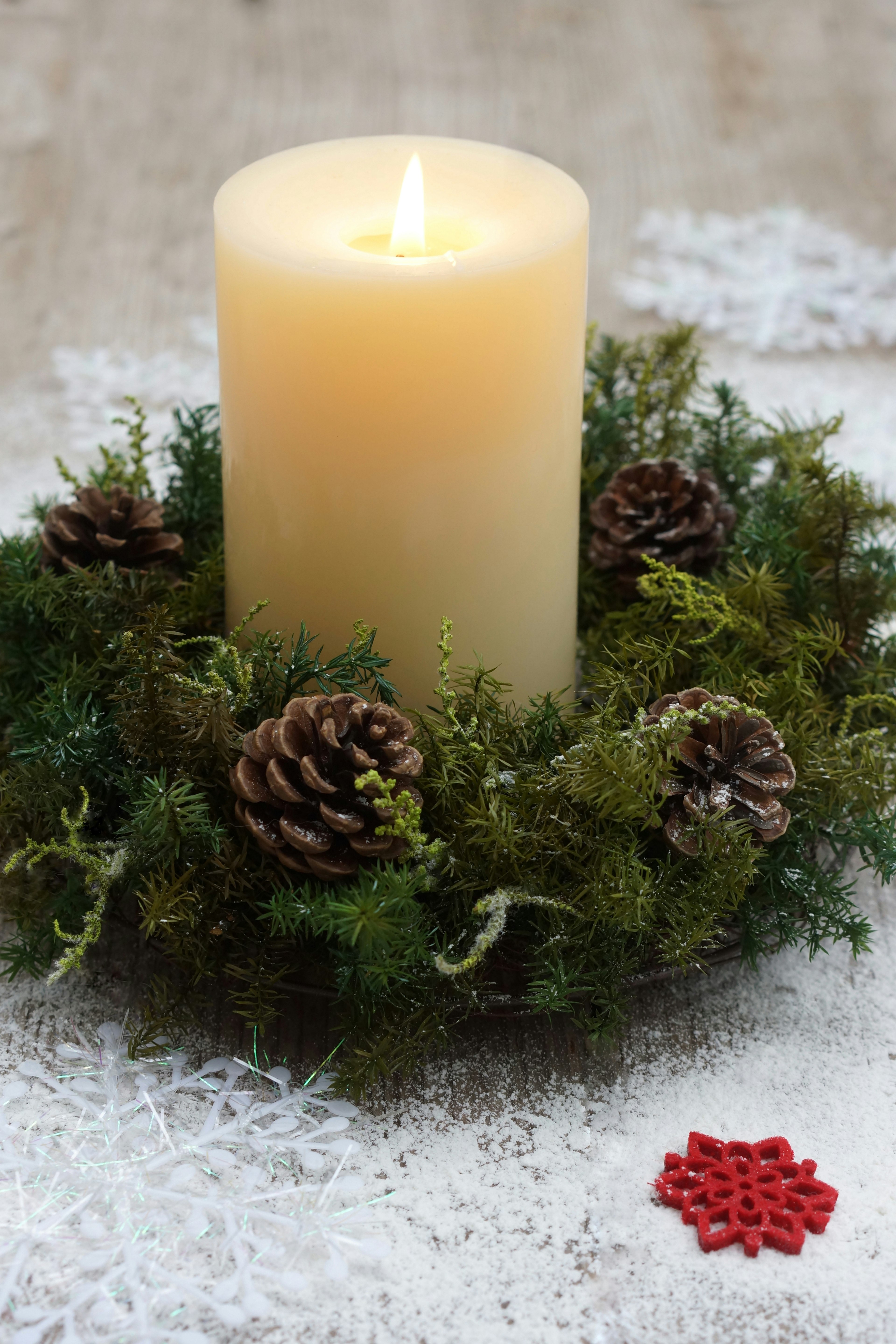 A lit candle surrounded by pine cones and moss in a festive wreath