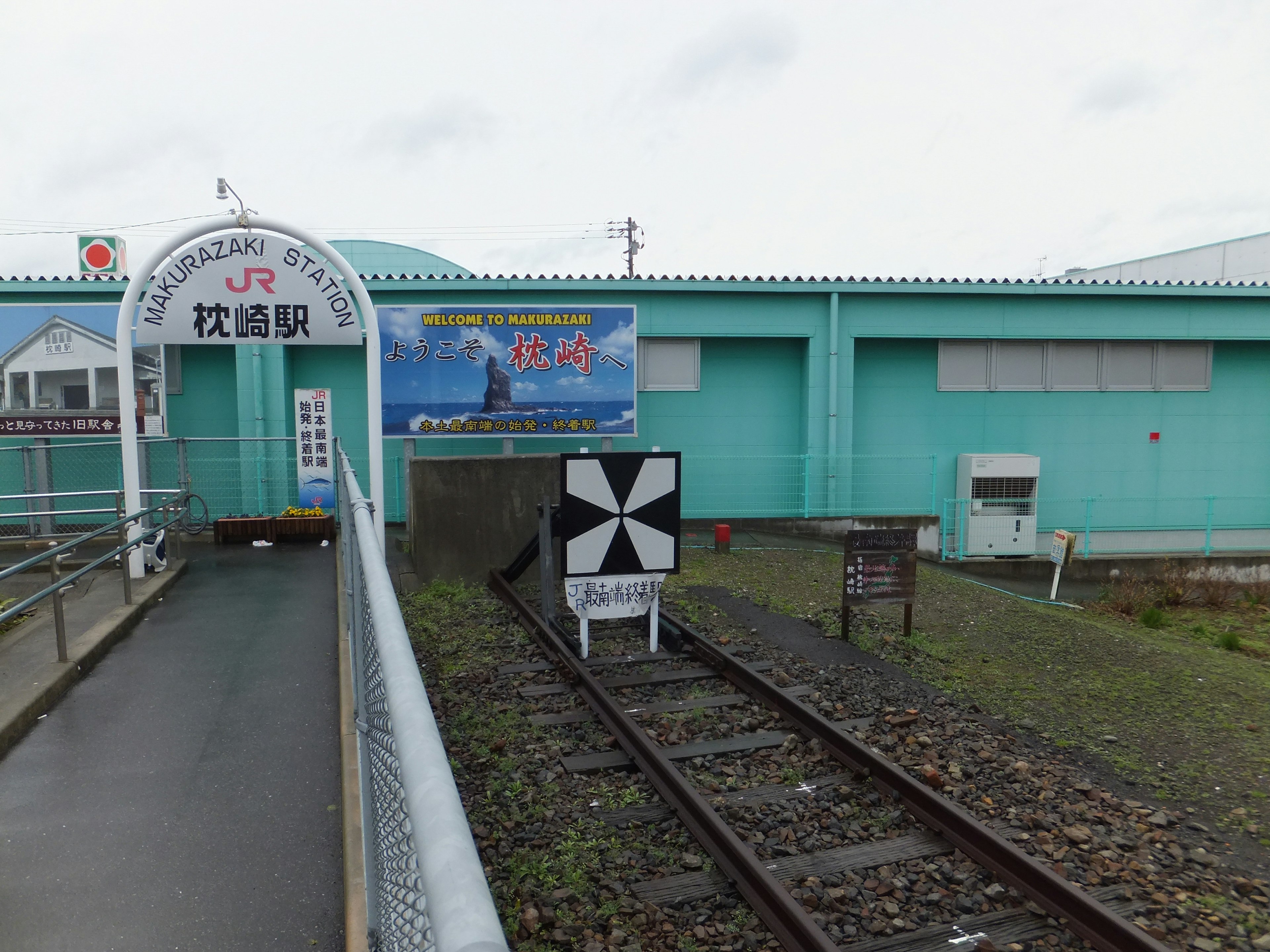 Bangunan stasiun hijau dengan rel di depan Nama stasiun adalah Matsushima Sinyal dan papan terlihat