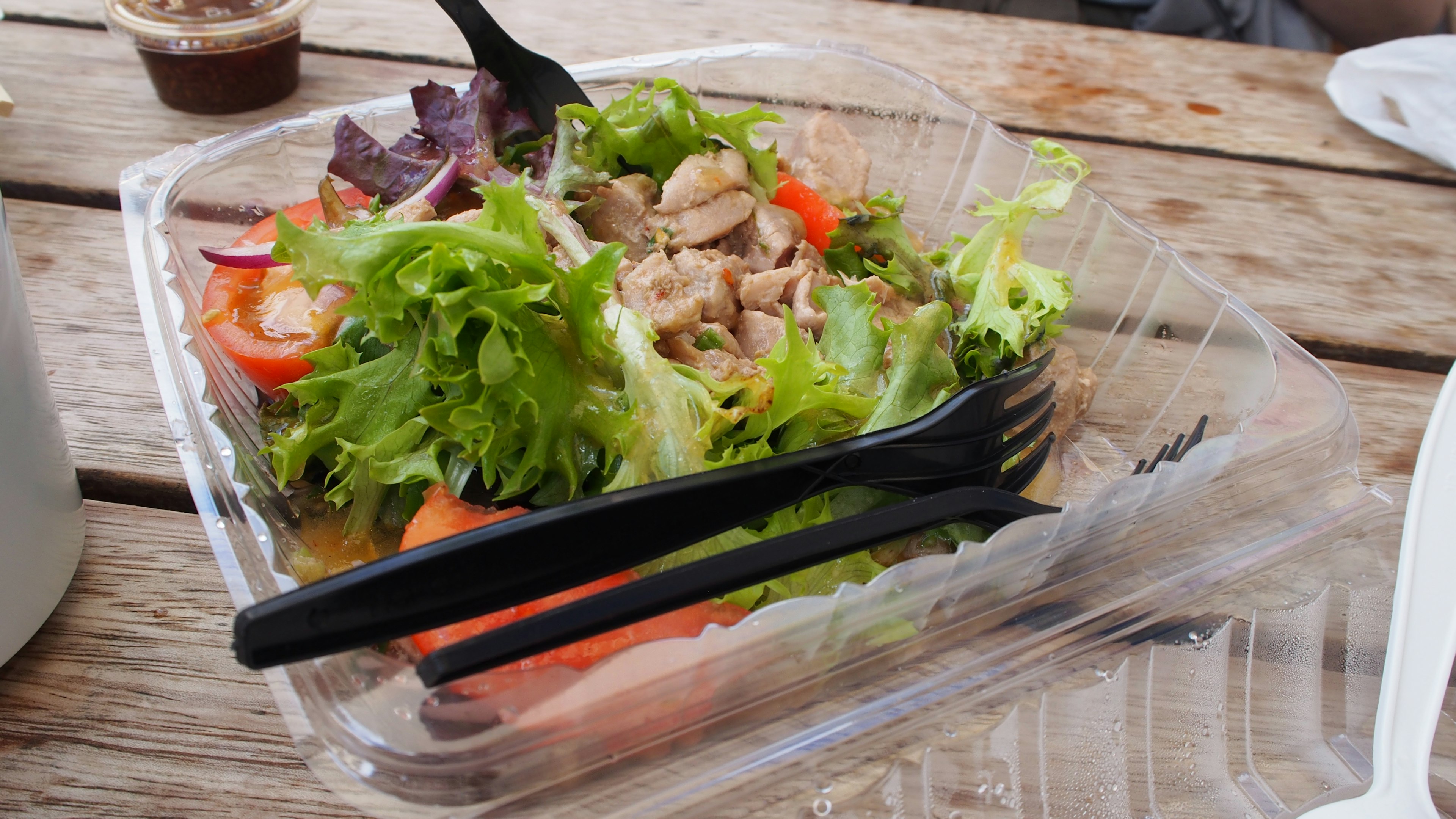 Foto de una ensalada en un recipiente transparente con lechuga tomates pollo y tenedores negros