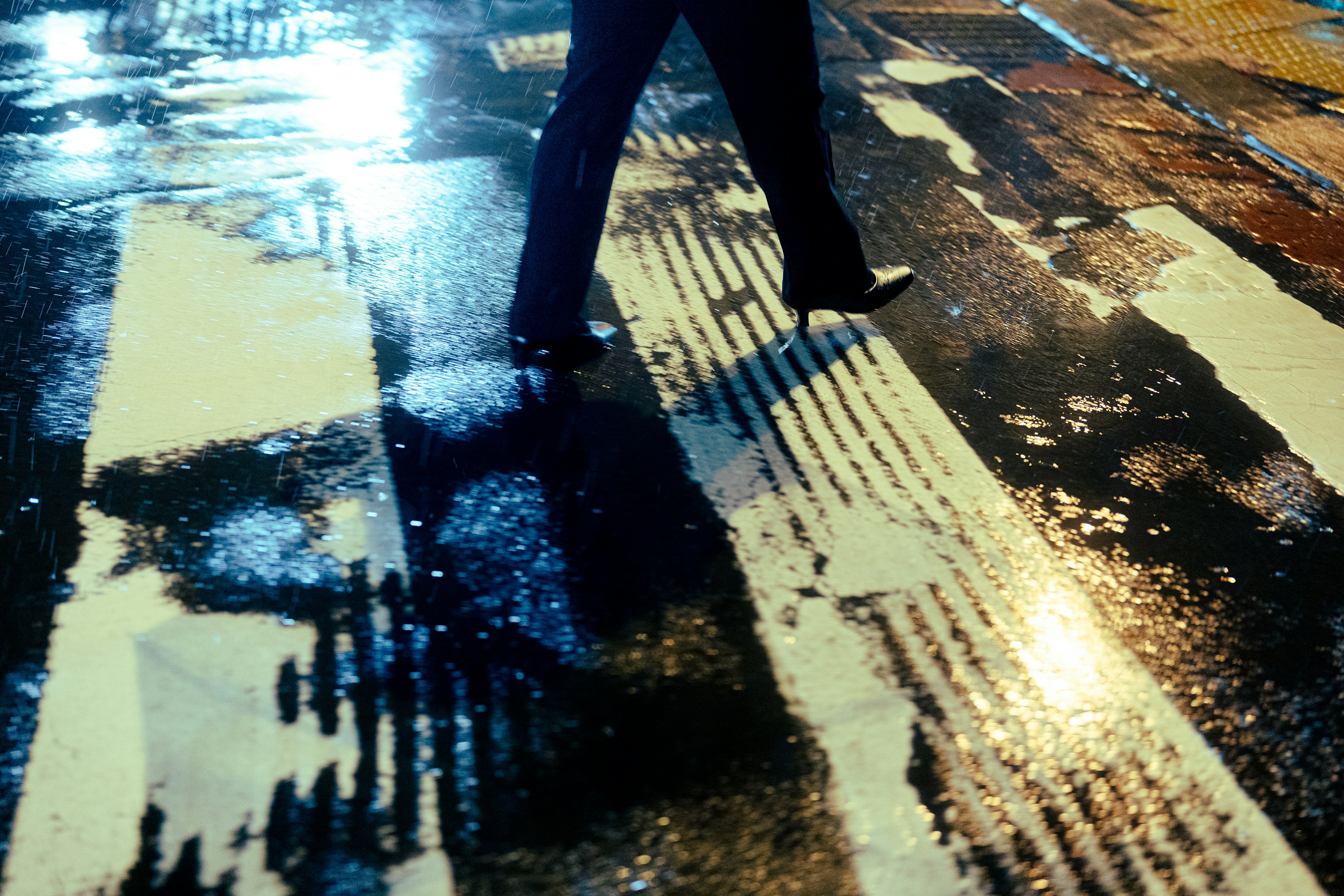 Silhouette of a person walking on a wet crosswalk at night with reflections