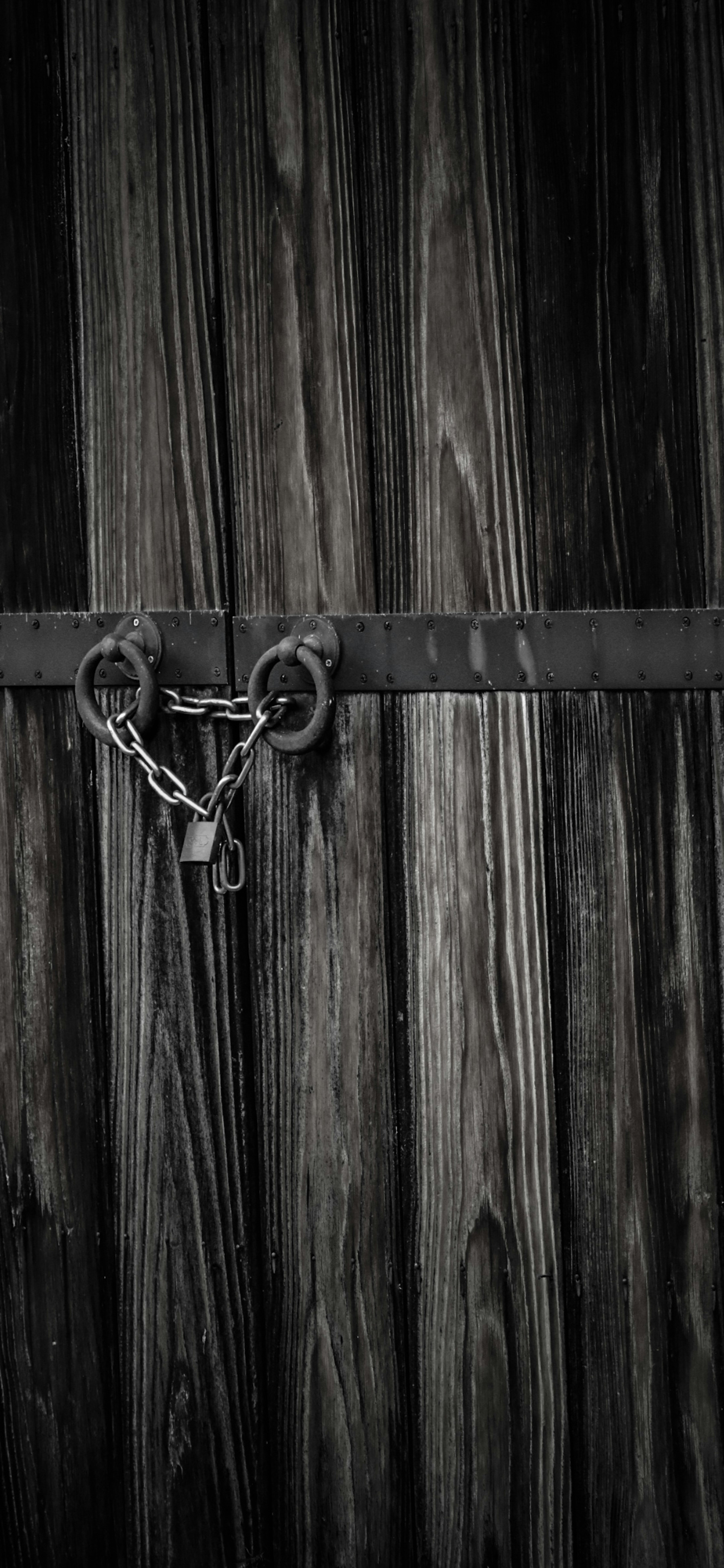 Close-up of a locked wooden door with chains and padlock