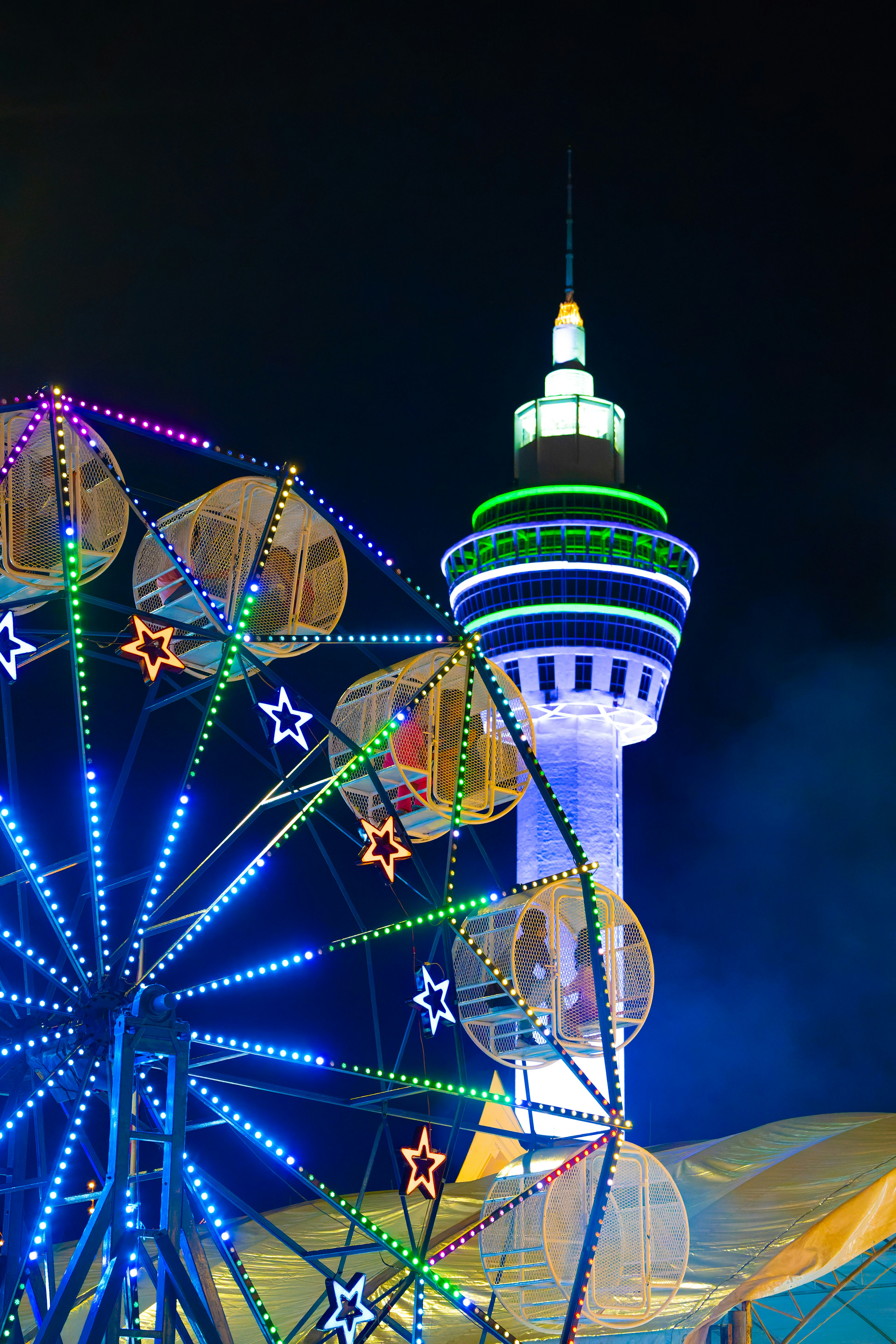 Luces coloridas iluminan una noria y una torre por la noche