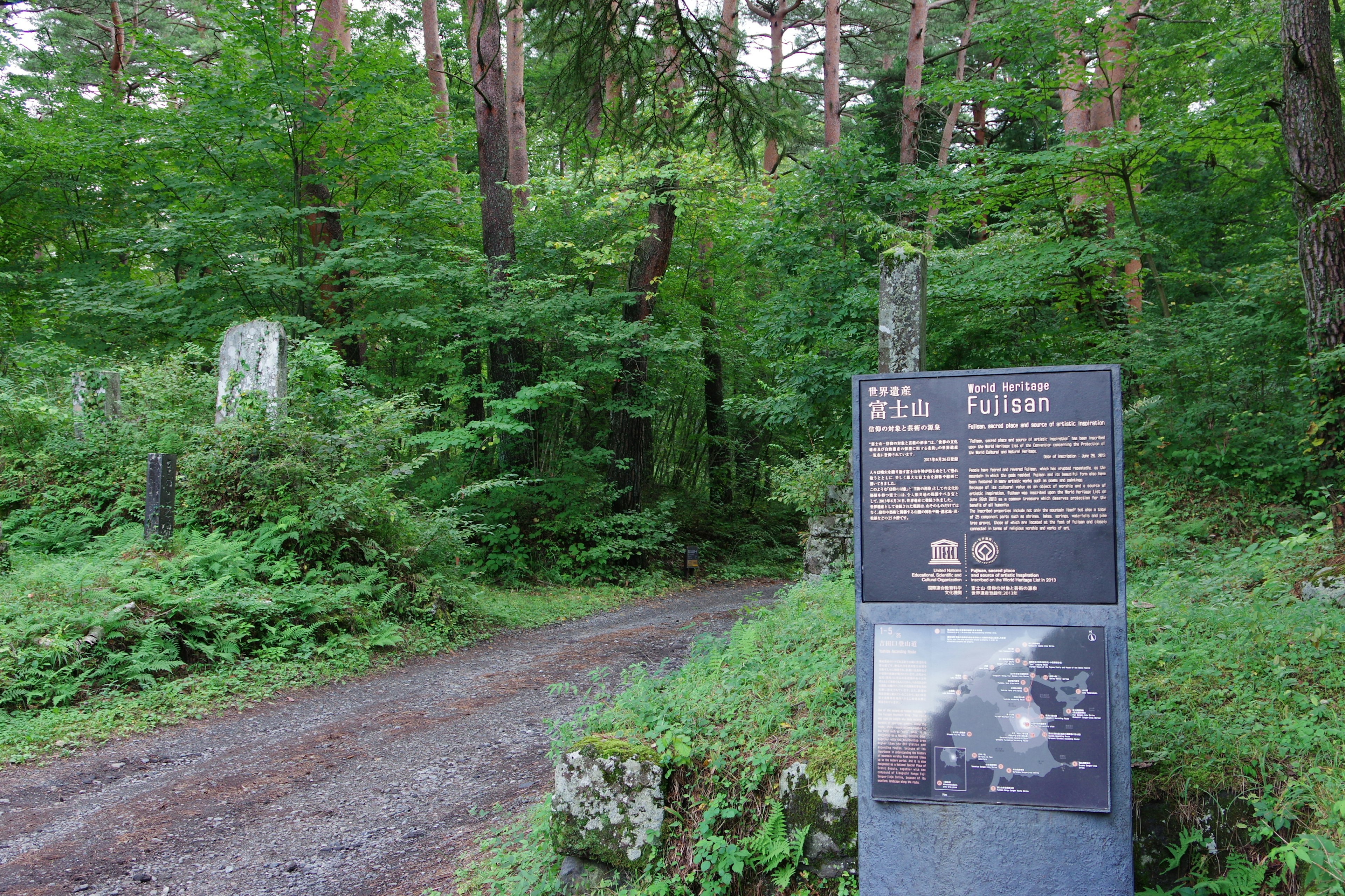 Schild und Steindenkmal in einem Wald umgeben von grünen Bäumen