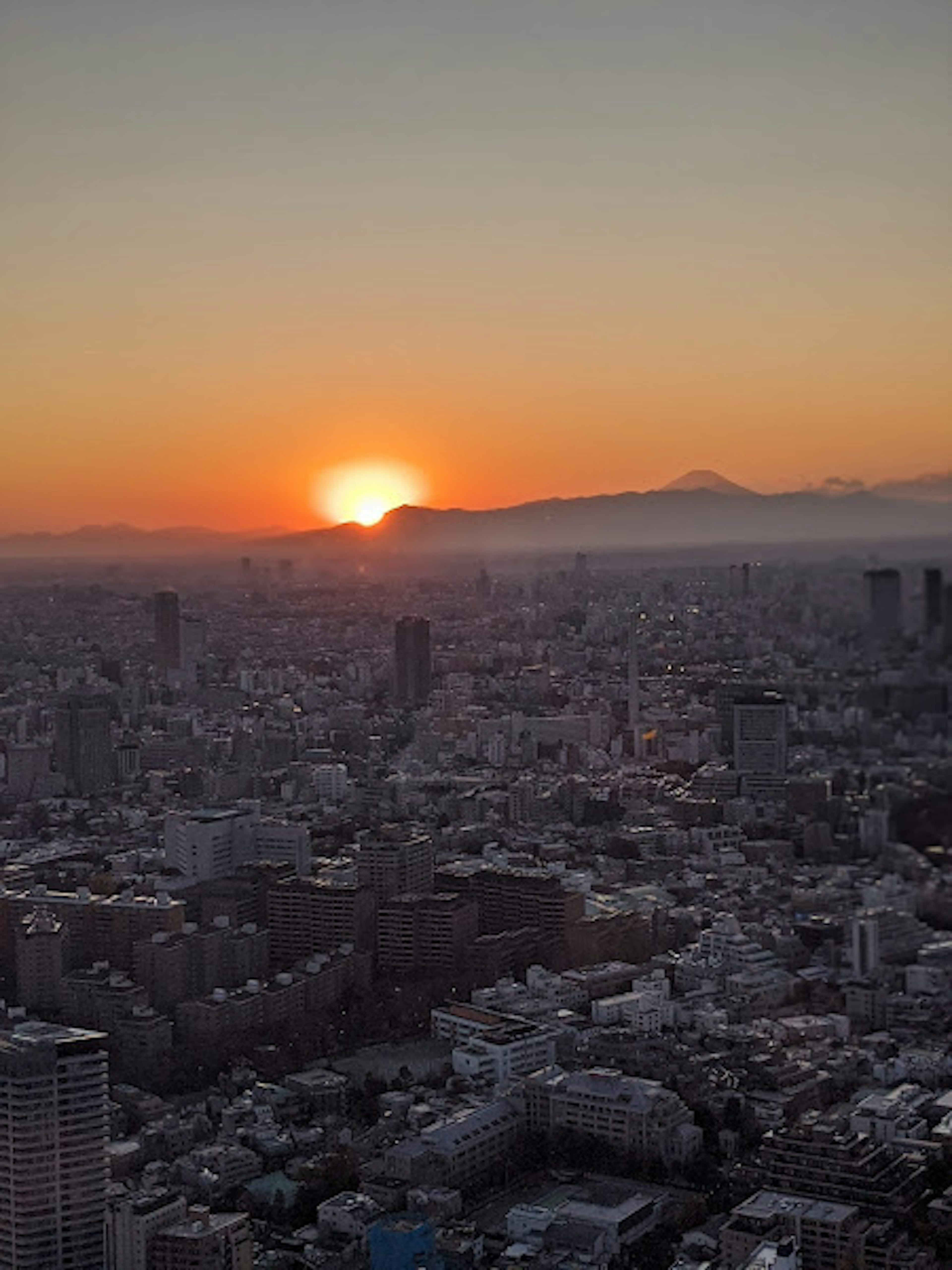 Stadtlandschaft von Tokio bei Sonnenuntergang mit Silhouetten von Wolkenkratzern und Bergen