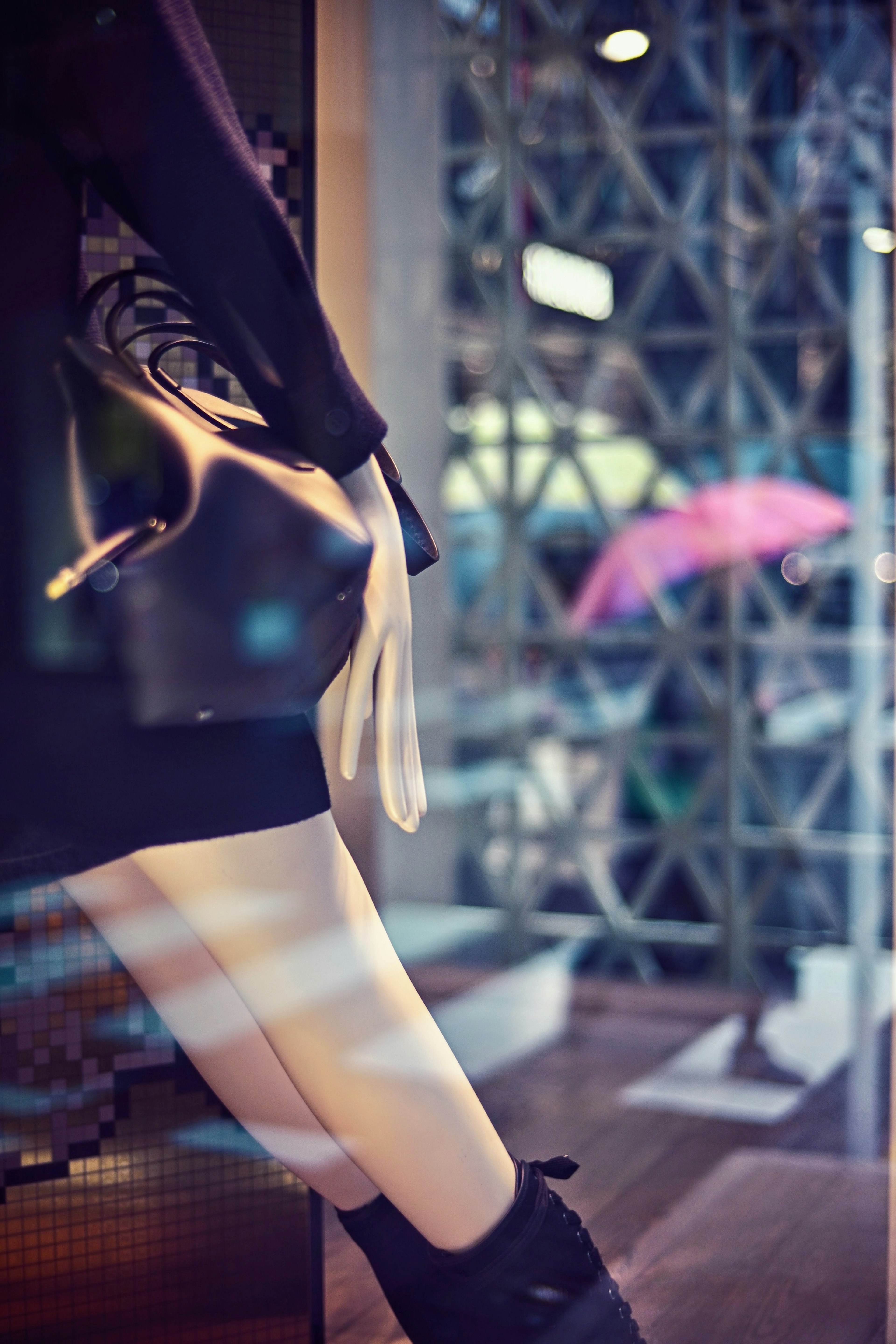 The leg of a mannequin dressed in a black outfit is displayed in a shop window with a colorful umbrella visible in the background