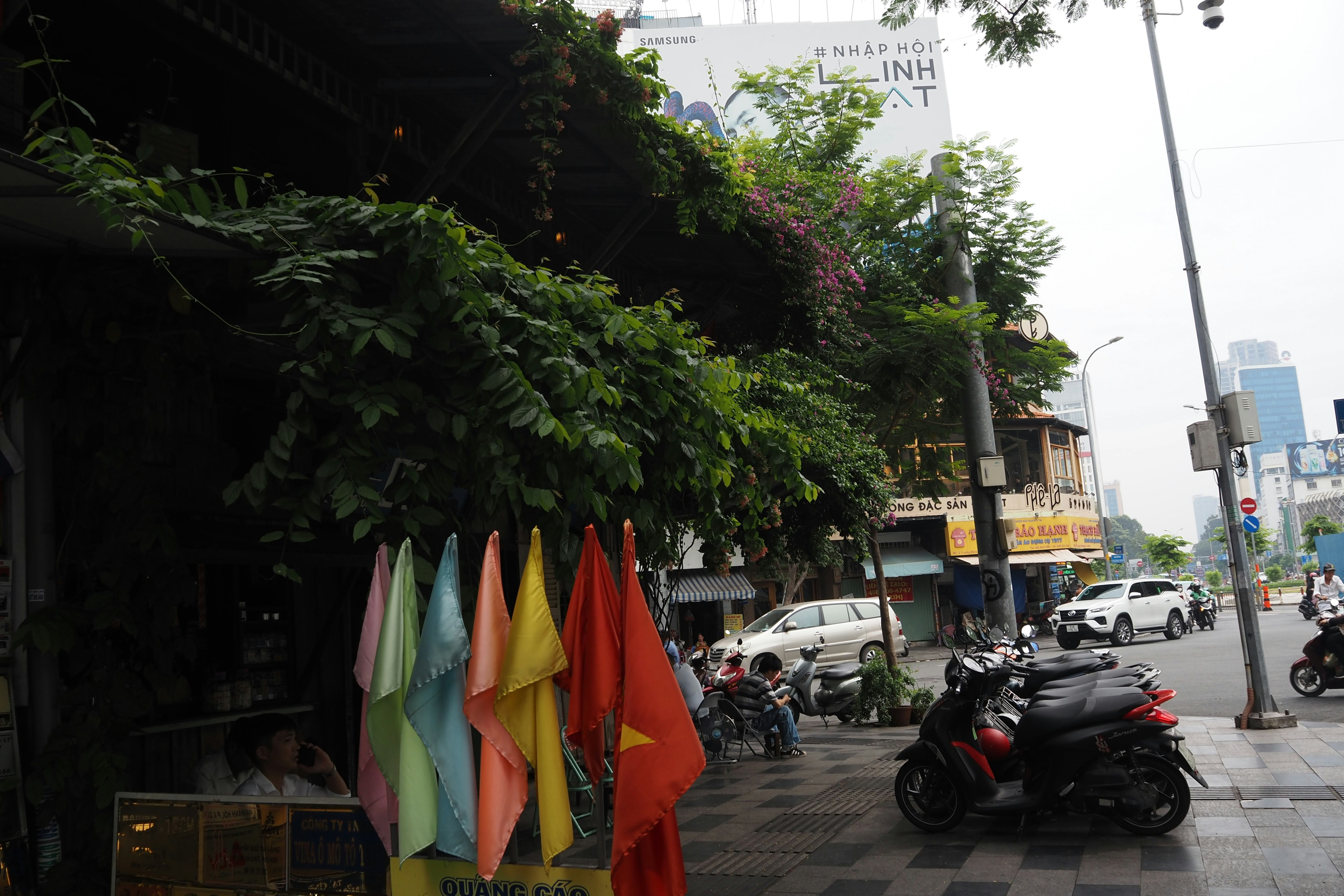 Banderas coloridas alineadas en una esquina de calle frondosa con motos