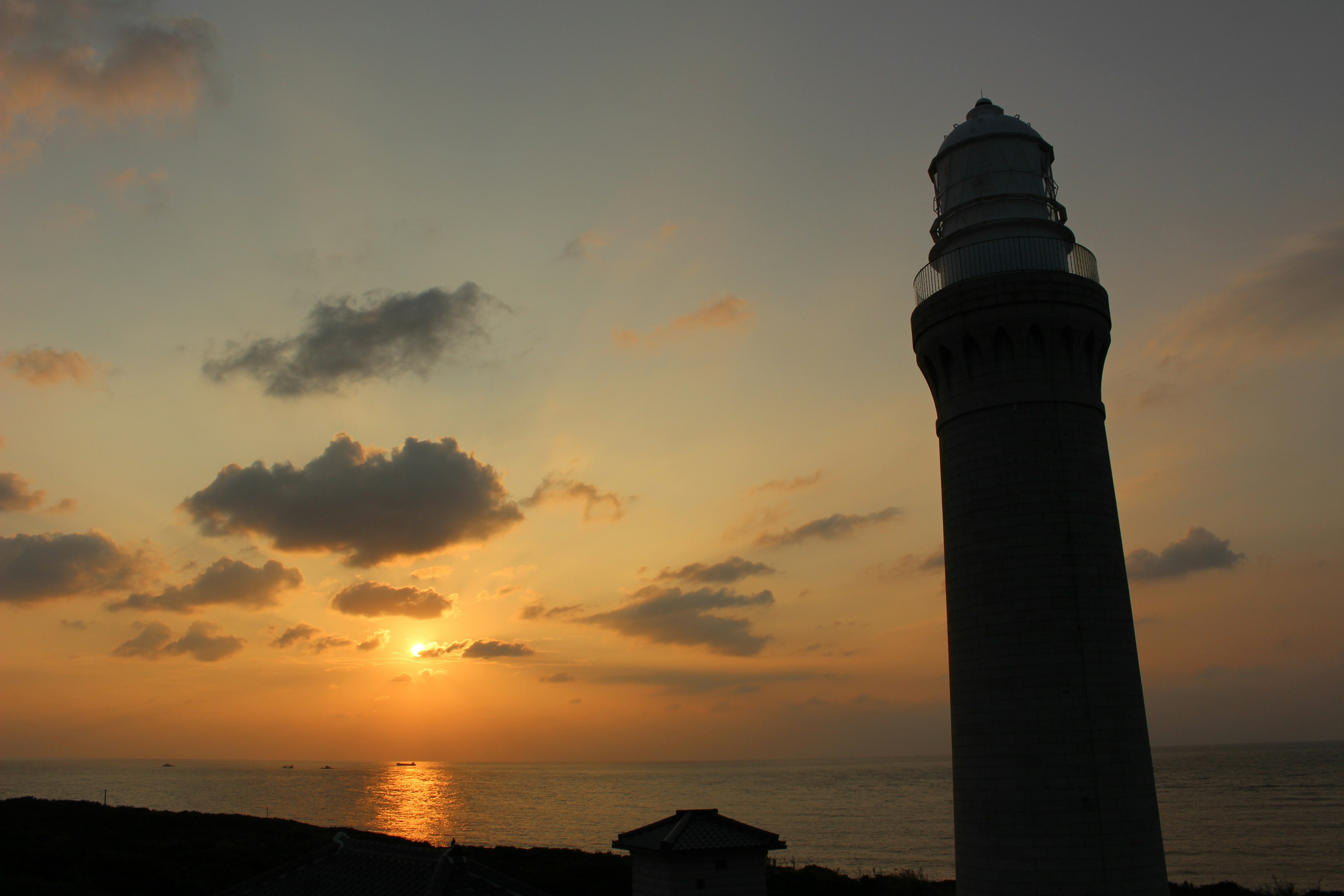 Silhouette of a lighthouse against a sunset over the ocean