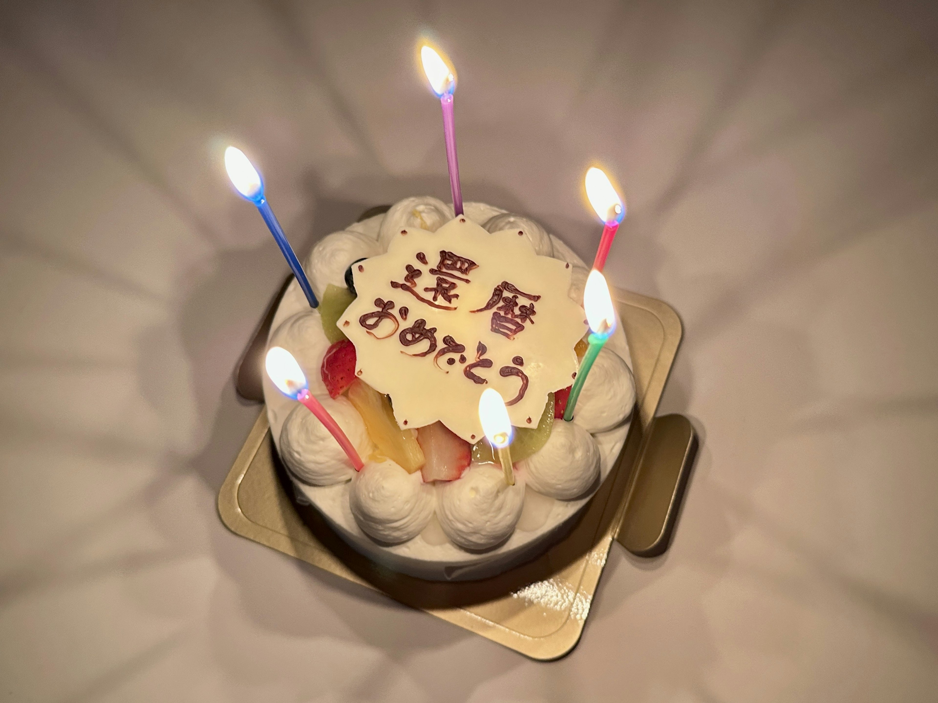 カラフルなろうそくが立てられた誕生日ケーキに"おめでとう"と書かれたプレート