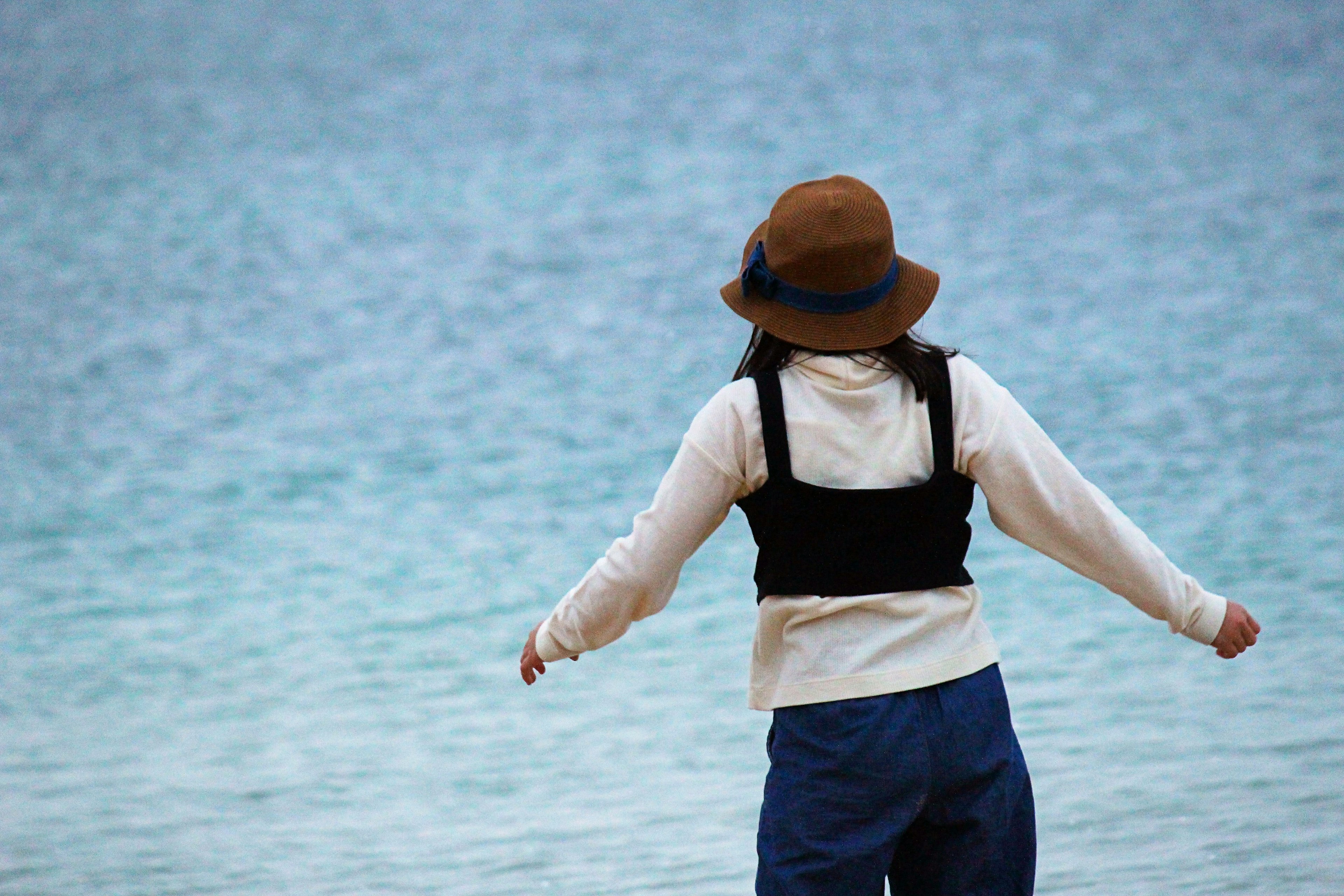 Donna in piedi al mare con un cappello marrone e abbigliamento casual