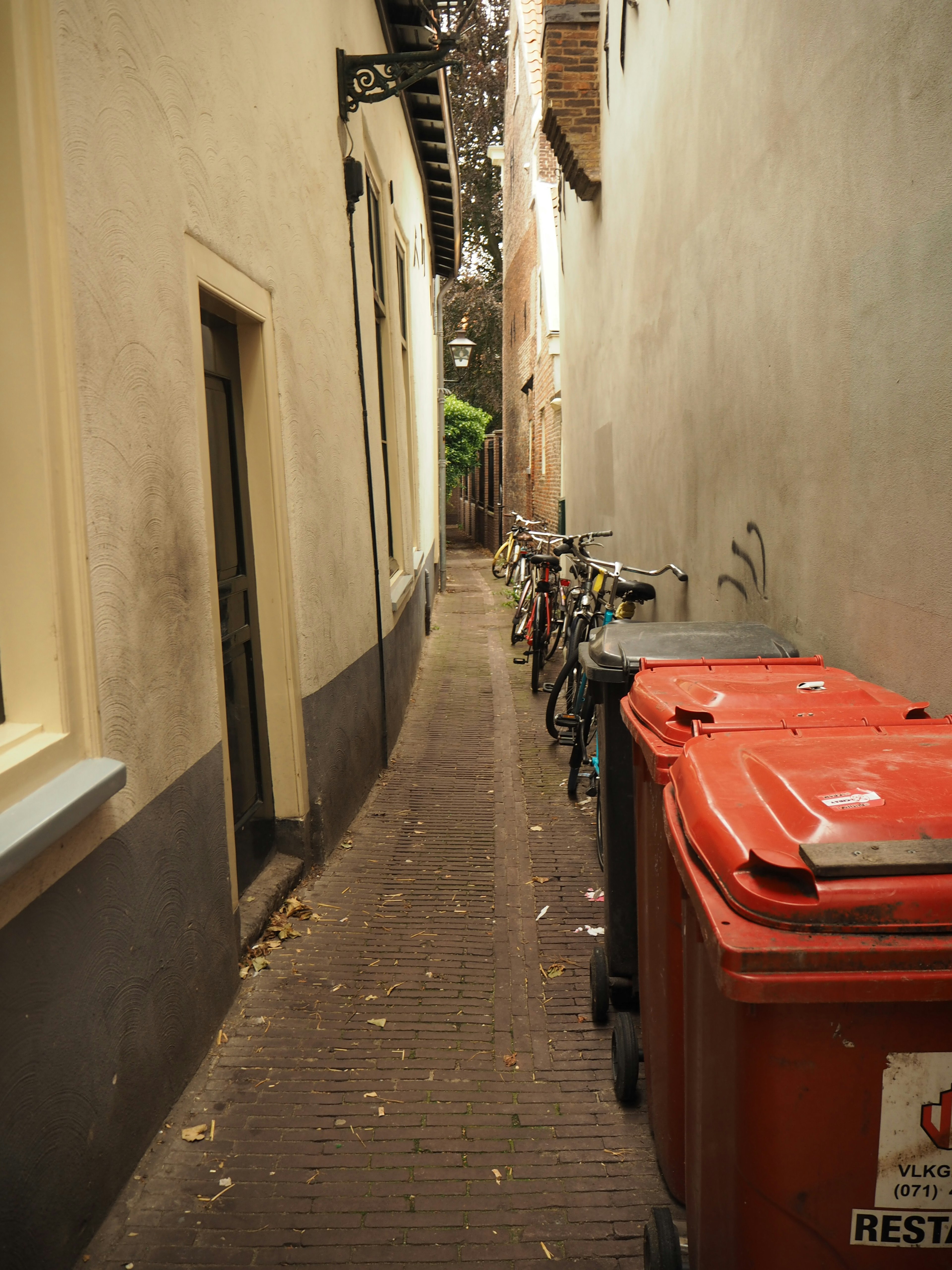 Narrow alley lined with red trash bins and bicycles