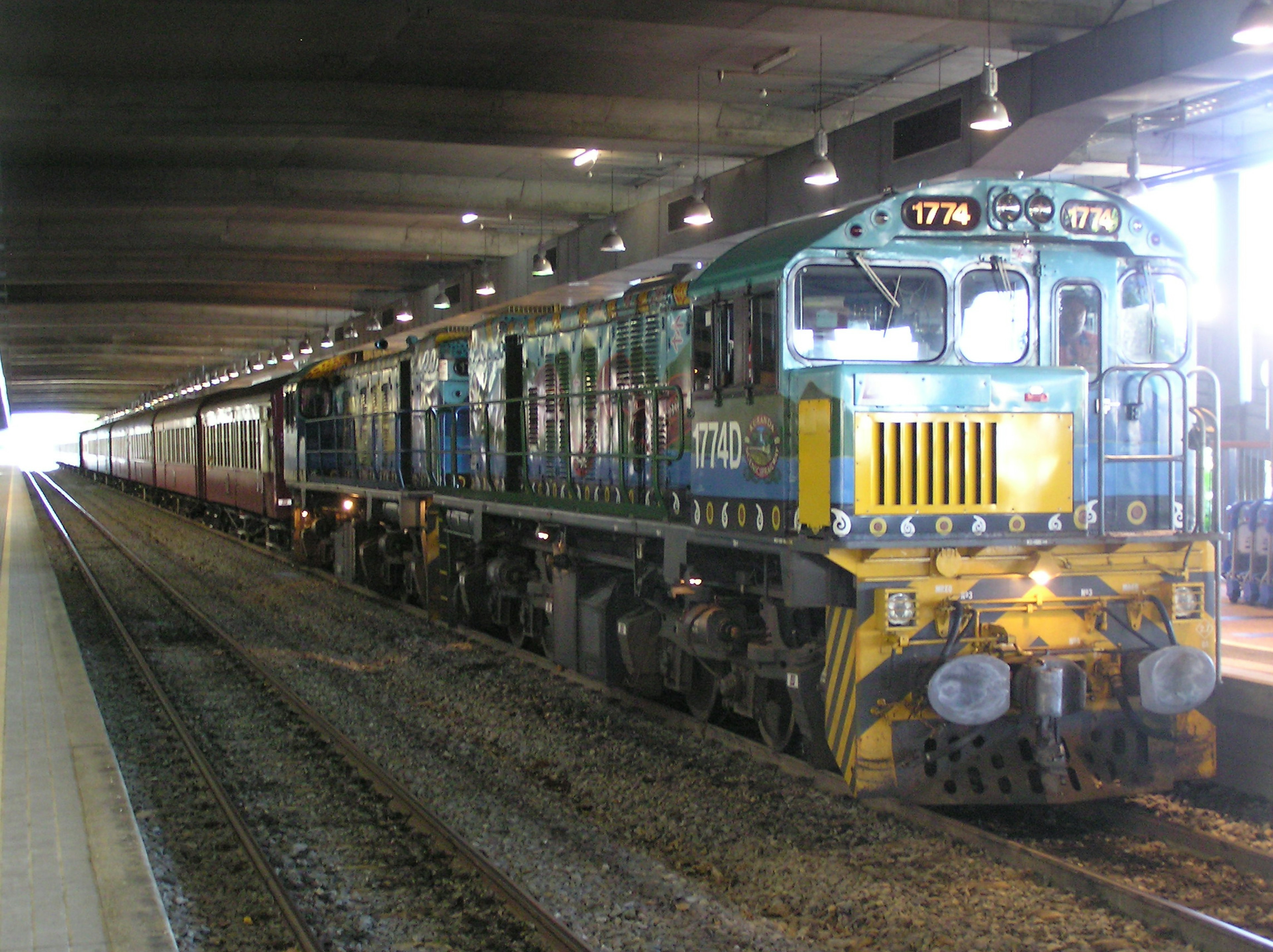 Locomotiva blu e gialla con carrozze passeggeri in stazione