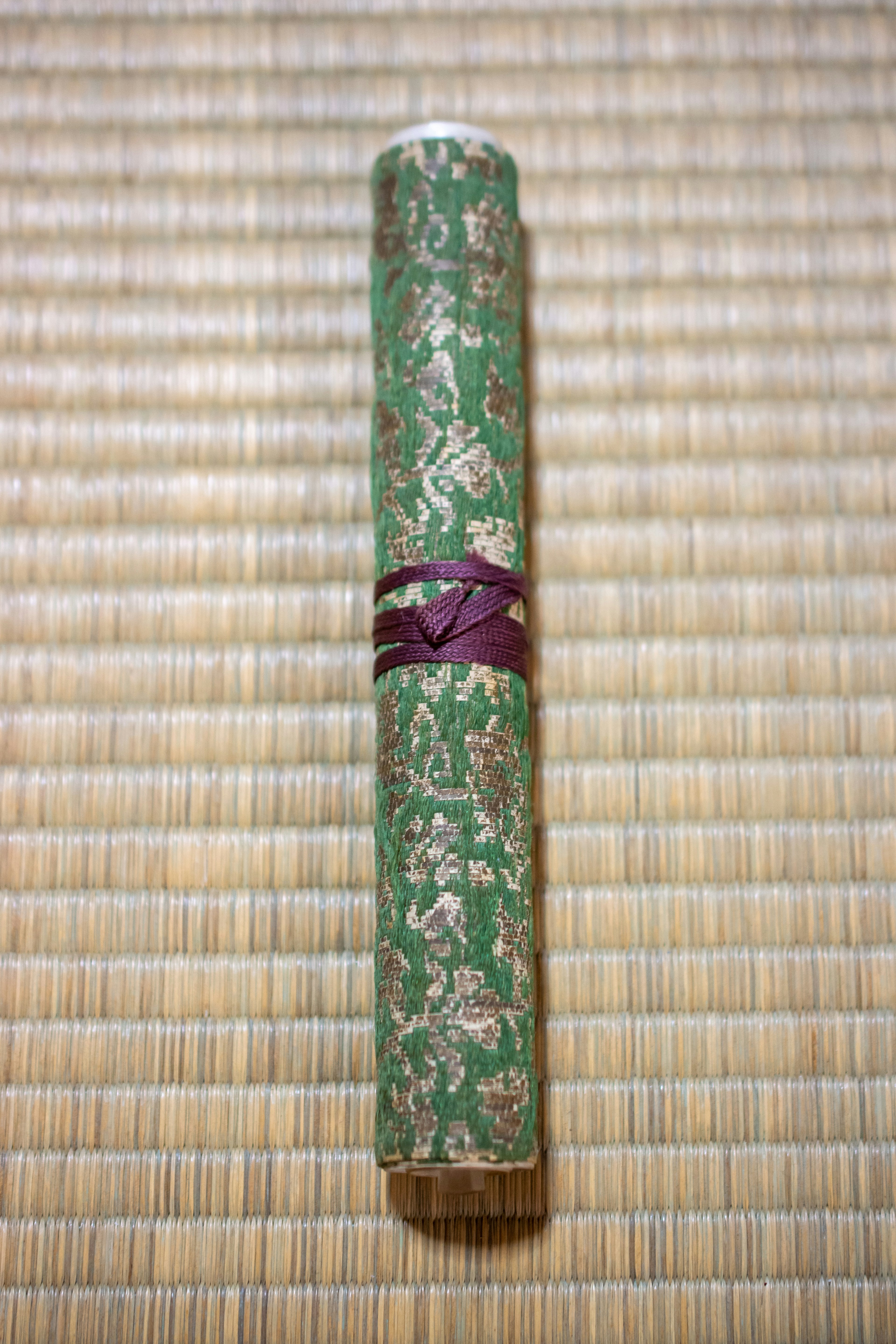 Traditional Japanese scroll with green patterned exterior secured by a purple ribbon