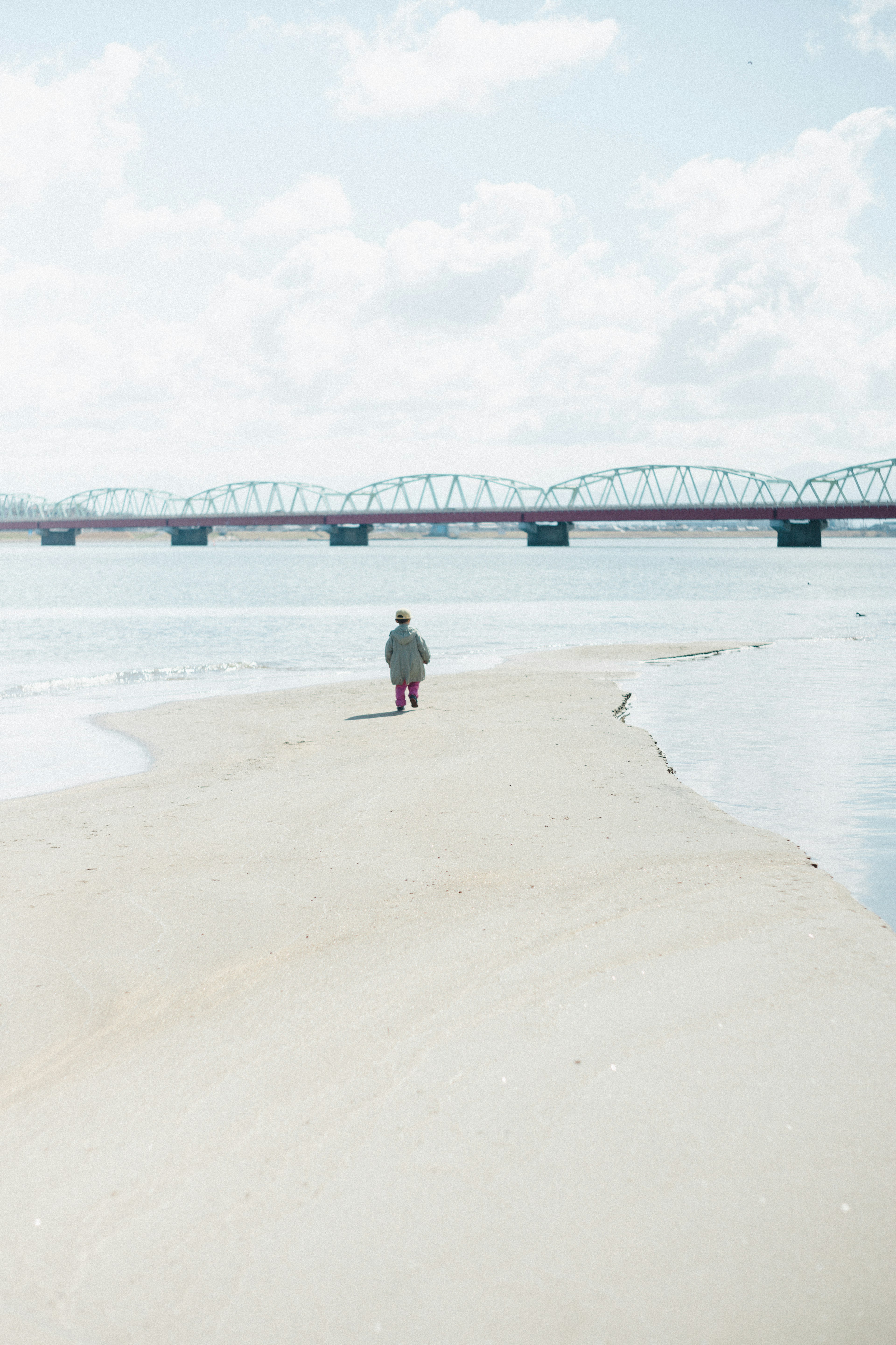 A person walking along a quiet riverbank with a bridge in the background