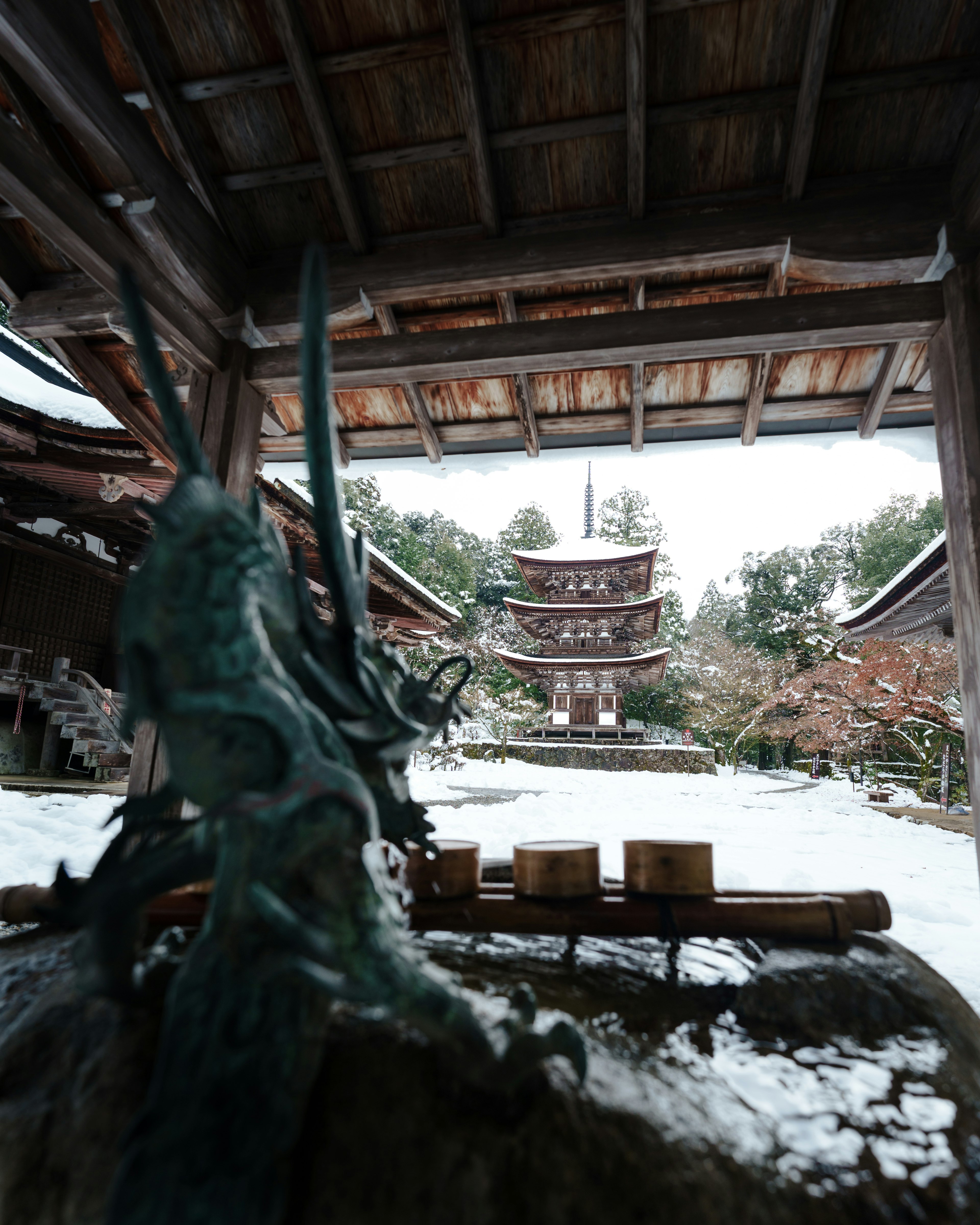 雪に覆われた古い日本の建物と青銅の彫刻が見える景色